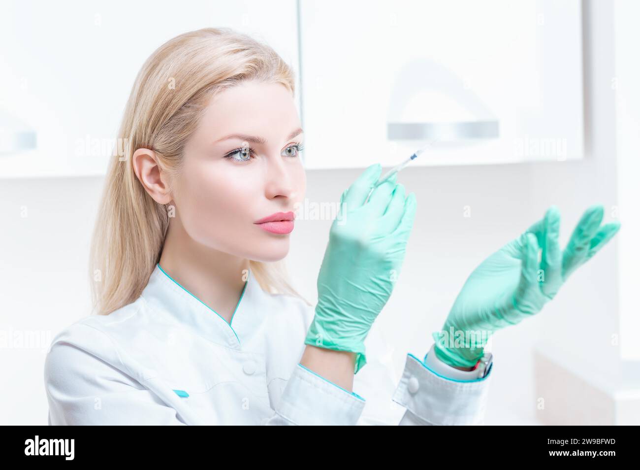 Ritratto di una ragazza bionda in abito medico con una siringa in mano. Pubblicità del centro medico. Supporti misti Foto Stock