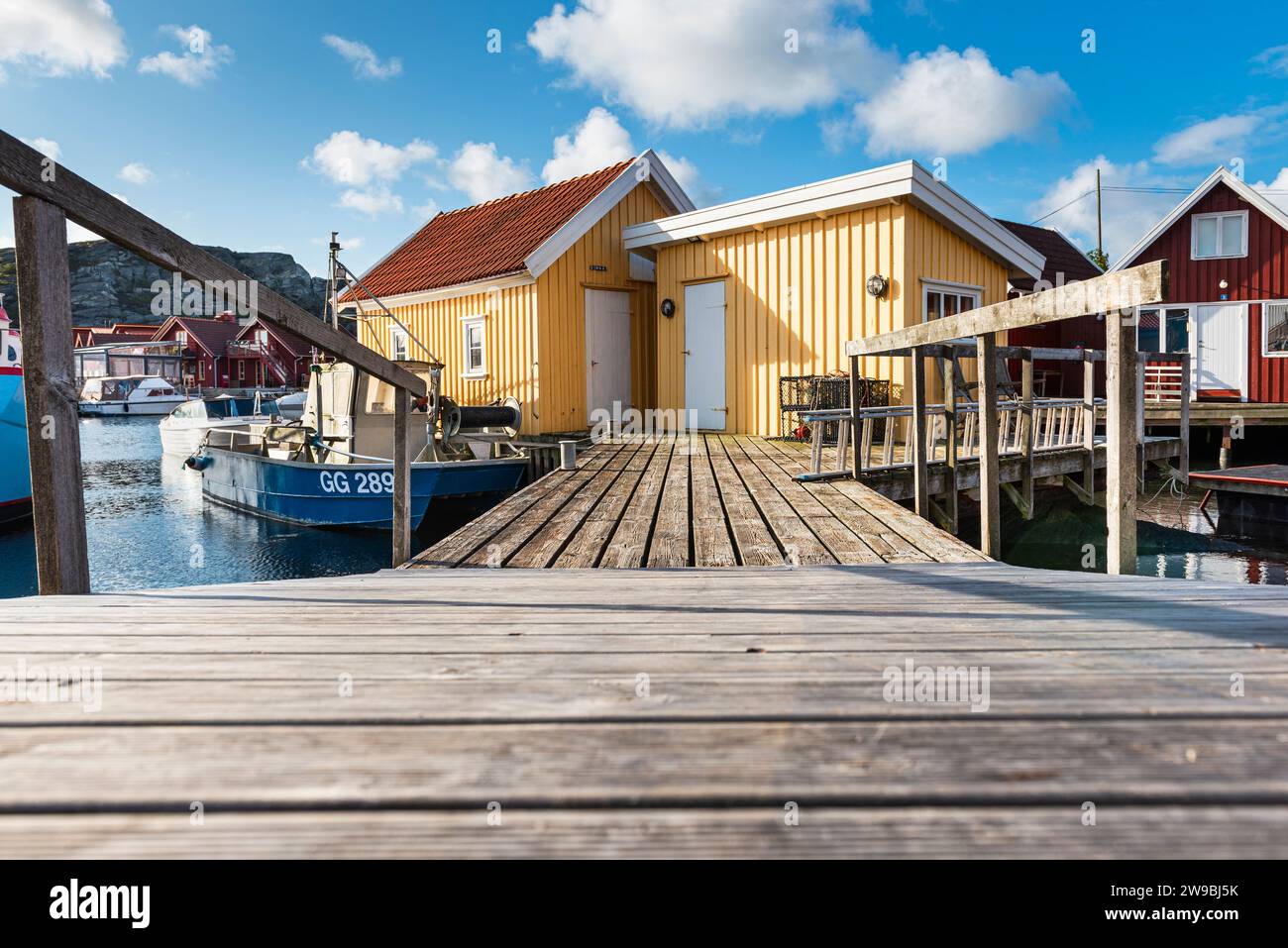 Barche da pesca presso il molo di legno del porto di fronte a una capanna gialla nel porto di Björholmen, nell'arcipelago dell'isola di Tjörn, Bohuslän, Svezia Foto Stock
