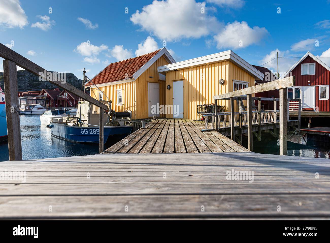 Barche da pesca presso il molo di legno del porto di fronte a una capanna gialla nel porto di Björholmen, nell'arcipelago dell'isola di Tjörn, Bohuslän, Svezia Foto Stock