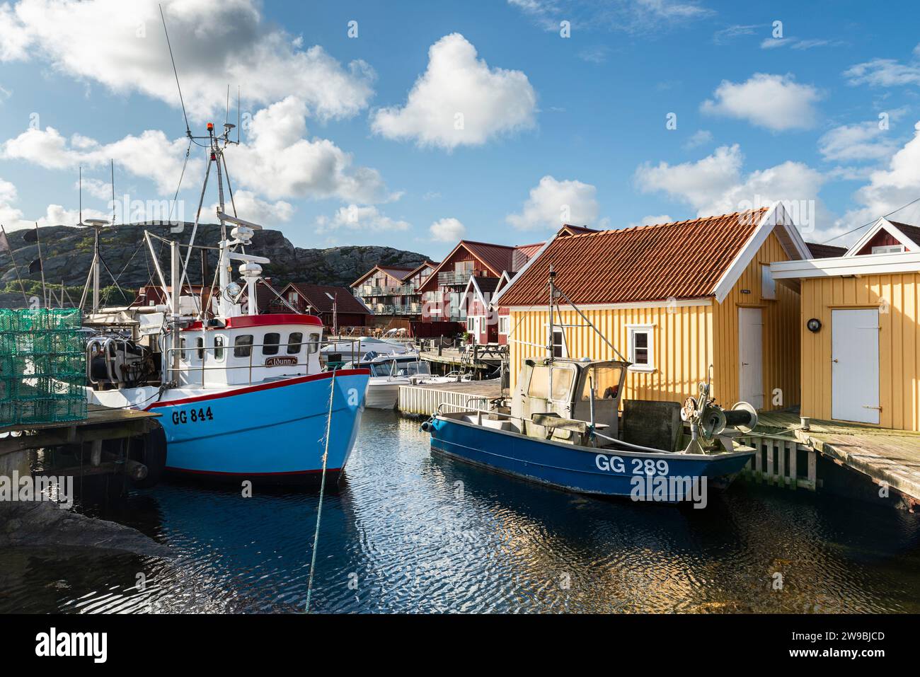 Barche da pesca presso il molo di legno del porto di fronte a una capanna gialla nel porto di Björholmen, nell'arcipelago dell'isola di Tjörn, Bohuslän, Svezia Foto Stock