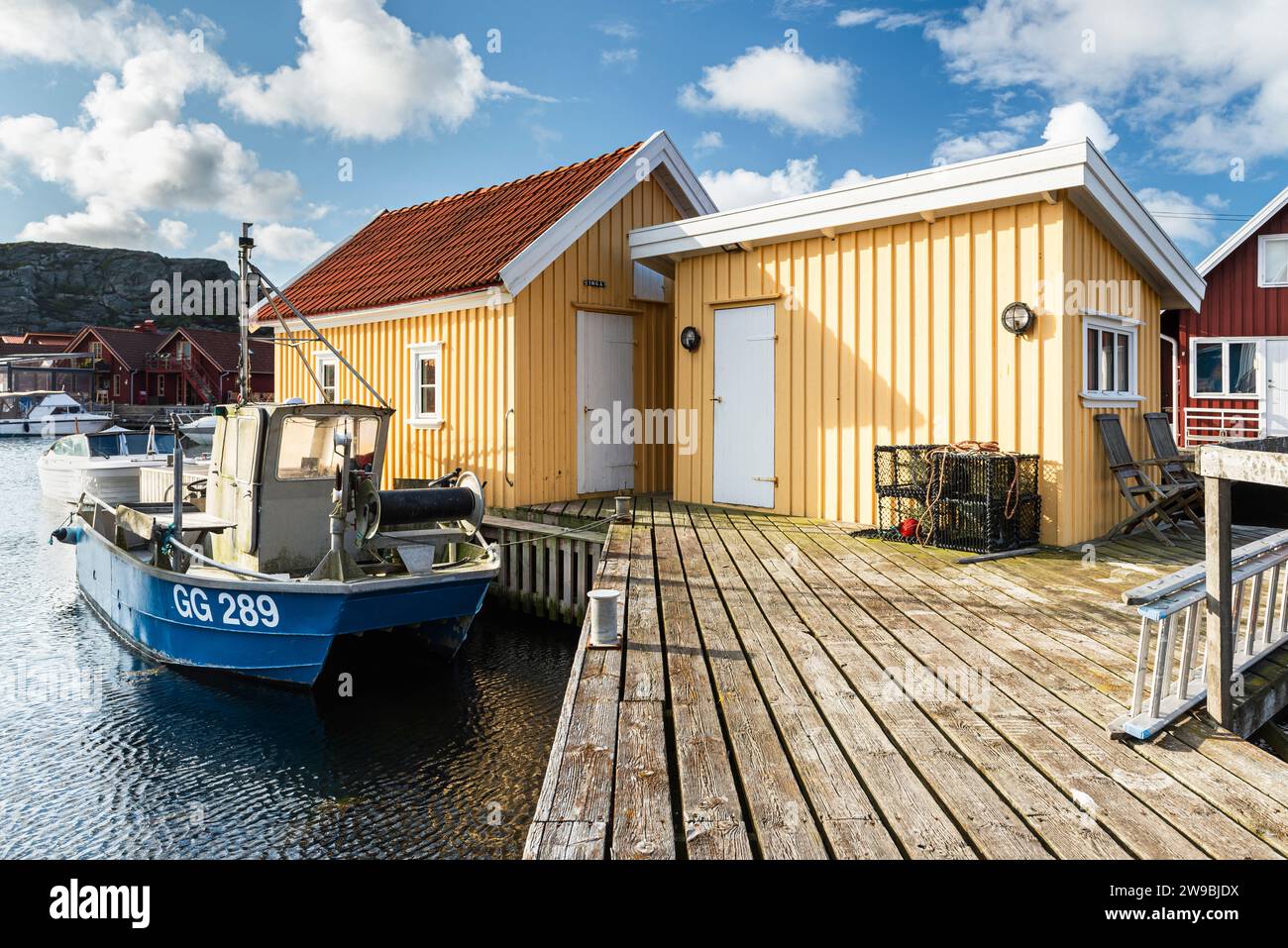 Barche da pesca presso il molo di legno del porto di fronte a una capanna gialla nel porto di Björholmen, nell'arcipelago dell'isola di Tjörn, Bohuslän, Svezia Foto Stock