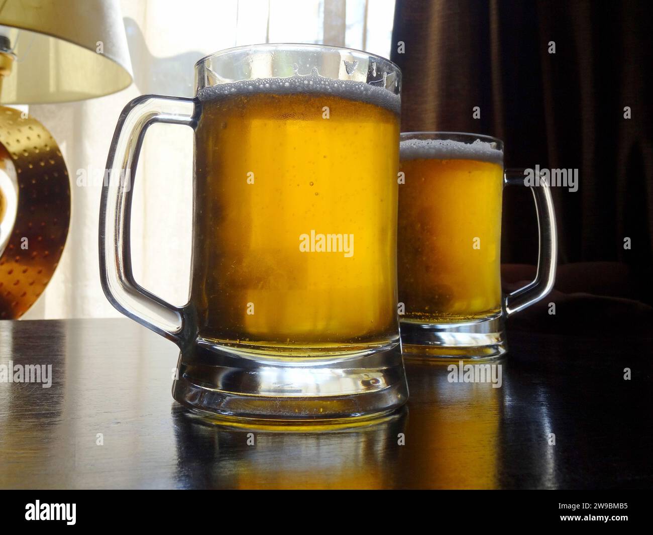 Birre alla spina complete sul tavolo di legno vicino alla finestra del pub Foto Stock