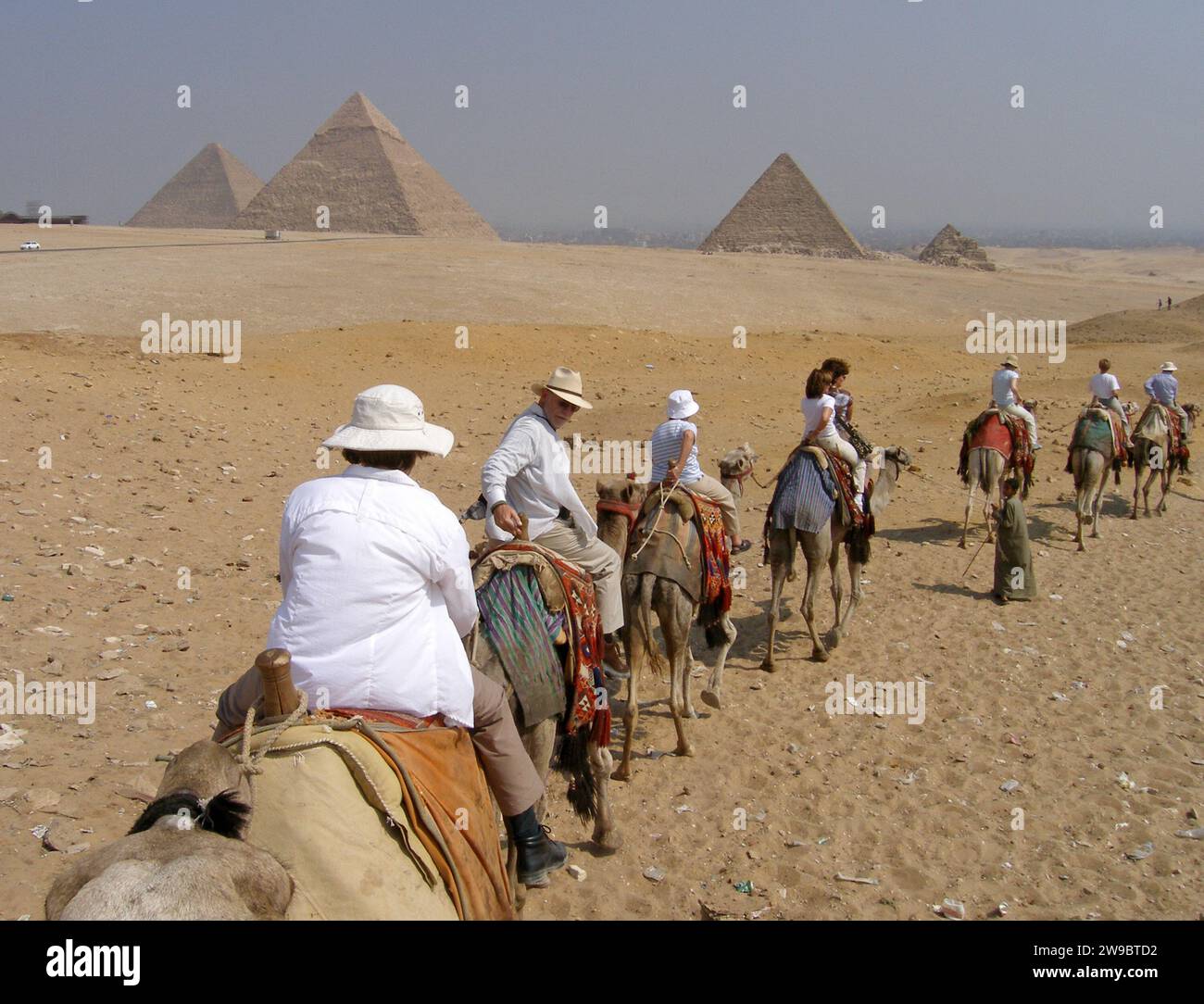 Una fila di turisti fa un giro a dorso di cammelli verso le piramidi dell'altopiano di Giza, vicino al Cairo, in Egitto. Foto Stock