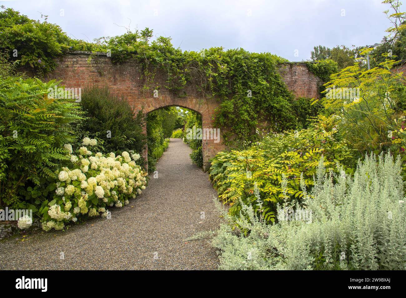 Arco in mattoni su un bellissimo sentiero con giardino all'inglese Foto Stock