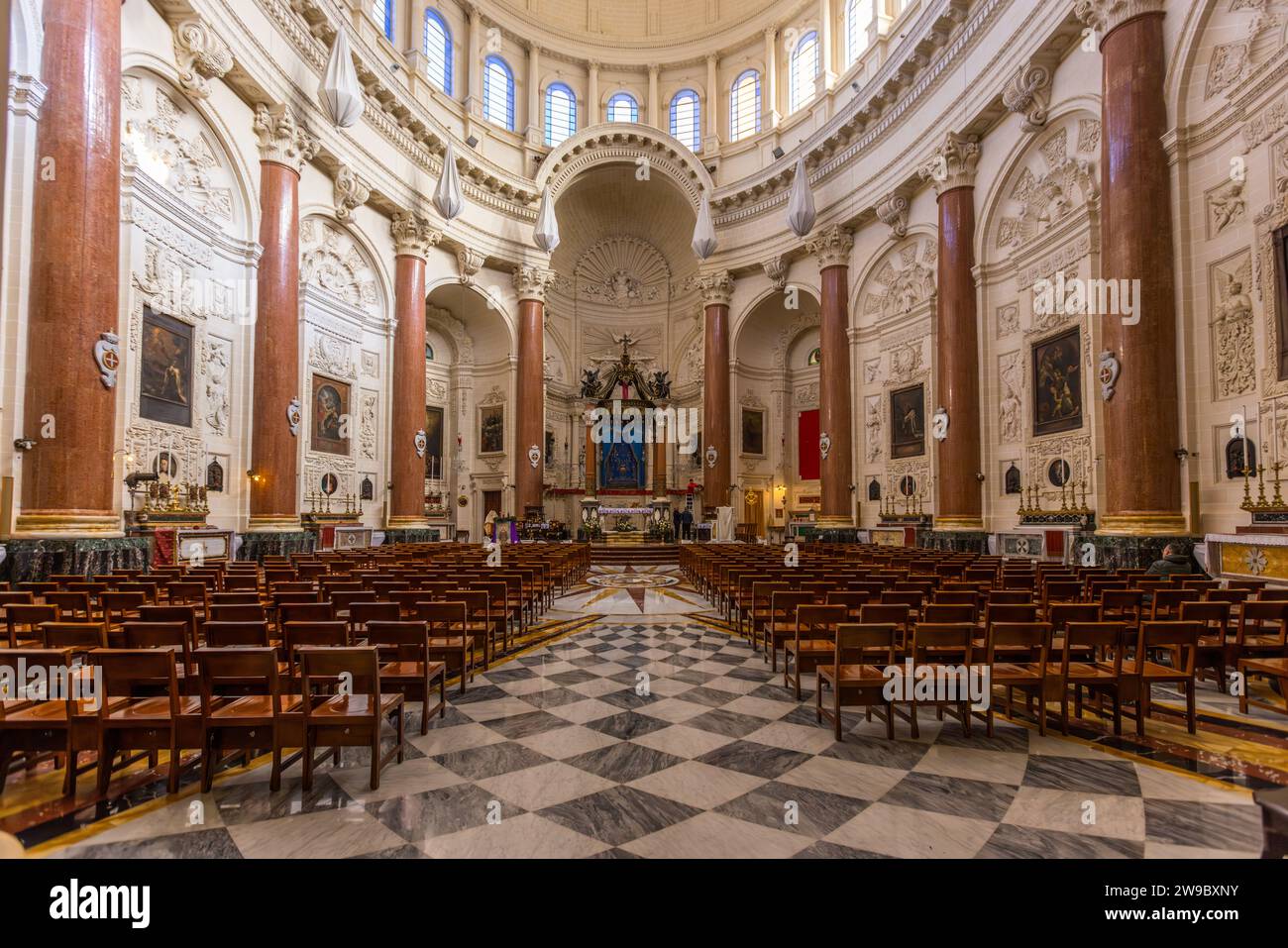 L'interno della chiesa carmelitana Bażilika Santwarju tal-Madonna tal-Karmnu (Basilica di Nostra Signora del Monte Carmelo) a La Valletta, Malta, mostra dei banchi su un pavimento di marmo a scacchi. I bombardamenti bellici distrussero quasi tutta la chiesa originale il 4 marzo 1942; l'attuale edificio, progettato dall'architetto Ġużè Damato, fu costruito tra il 1958 e il 1981, con una cupola alta 42 metri costruita deliberatamente leggermente più alta della vicina cattedrale pro-anglicana di San Paolo. Foto Stock