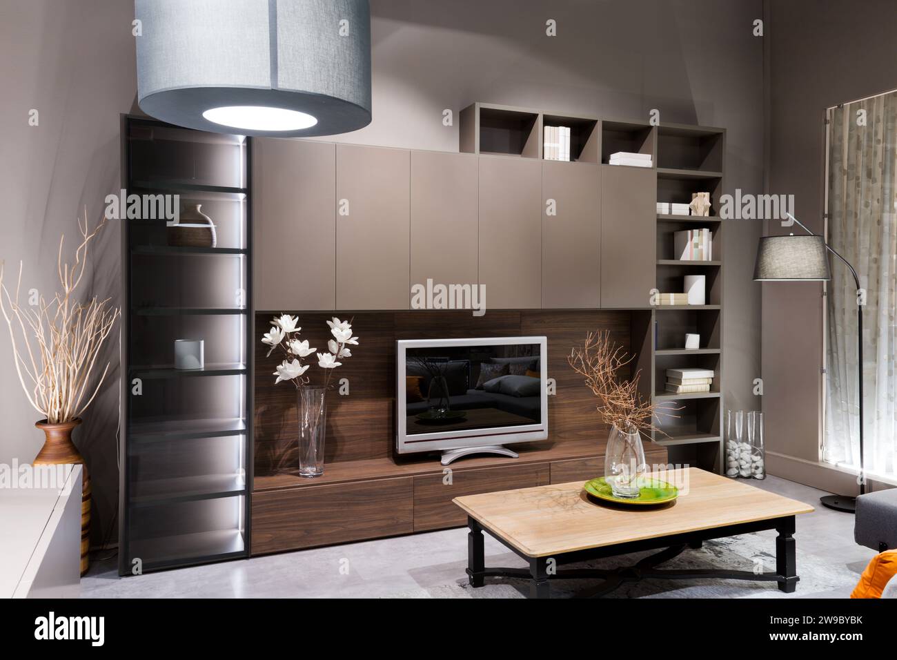 Design interno di un moderno soggiorno illuminato con tavolo e vaso in legno con fiori e televisore in mobili da scaffale a muro in legno su piano liscio Foto Stock
