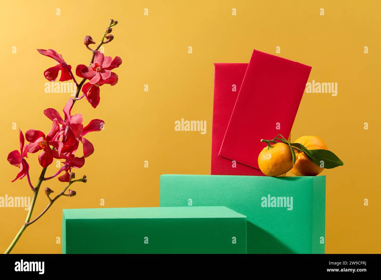 Buste rosse, vivaci orchidee e mandarini, il podio verde presenta i prodotti sullo sfondo giallo festoso, fornendo un ambiente ideale per un Foto Stock