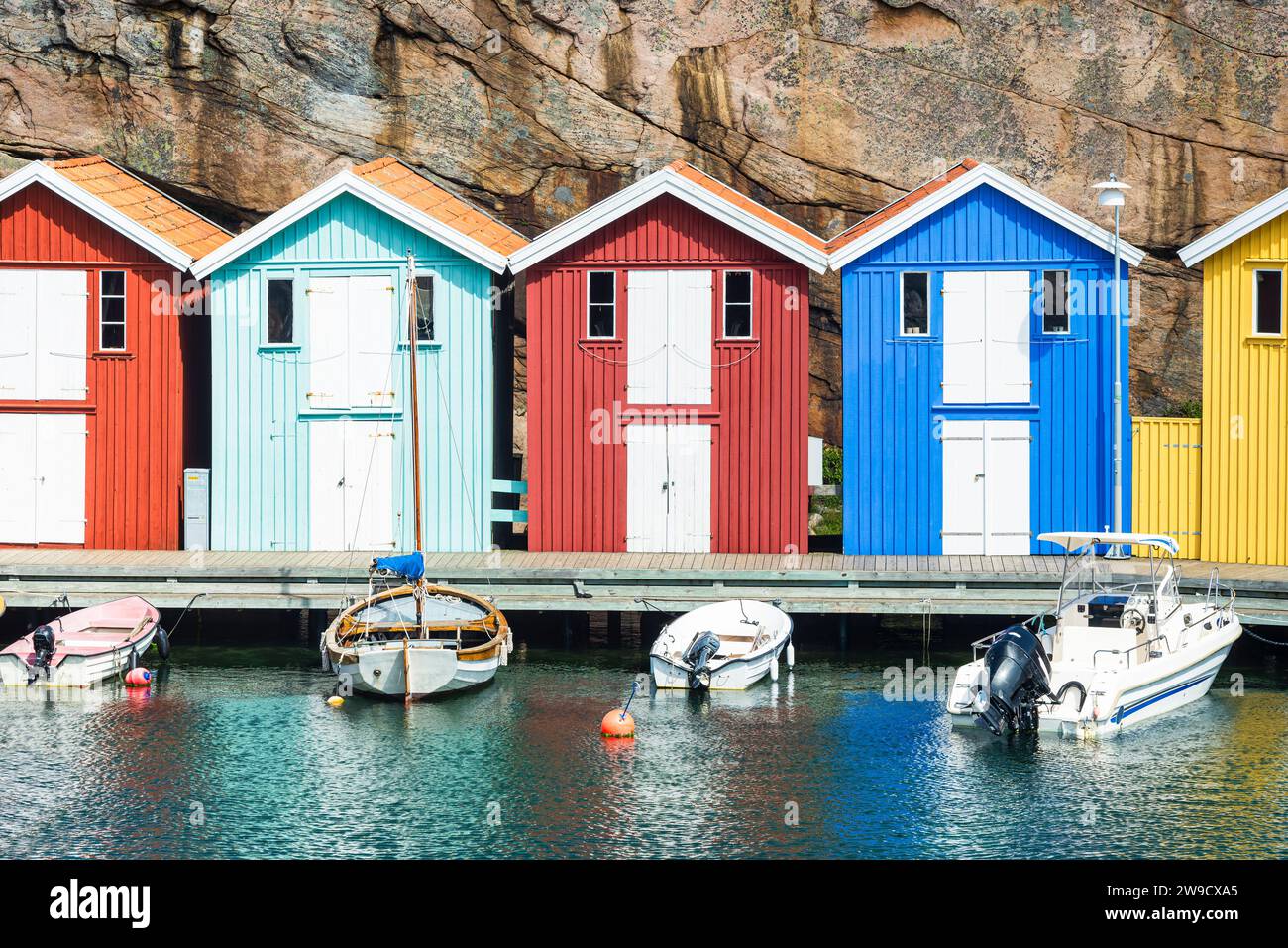 Capannoni per barche e magazzini con colorate facciate in legno e rocce di granito nel porto di Smögen, nell'arcipelago della costa occidentale svedese Foto Stock