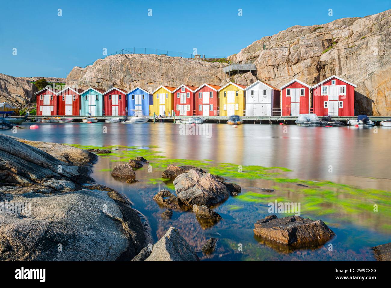 Capannoni per barche e magazzini con colorate facciate in legno e rocce di granito nel porto di Smögen, nell'arcipelago della costa occidentale svedese Foto Stock