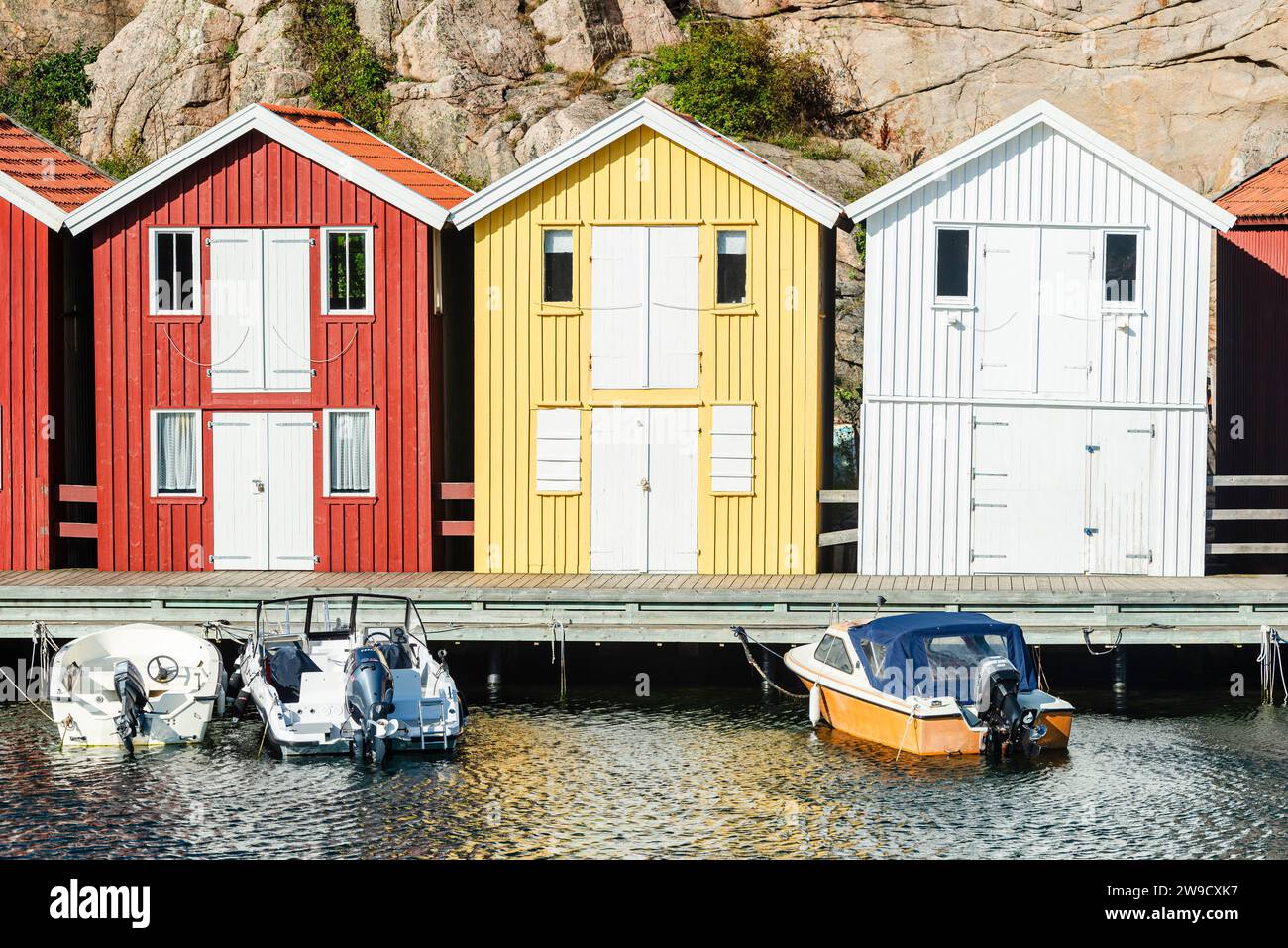 Capannoni per barche e magazzini con colorate facciate in legno e rocce di granito nel porto di Smögen, nell'arcipelago della costa occidentale svedese Foto Stock