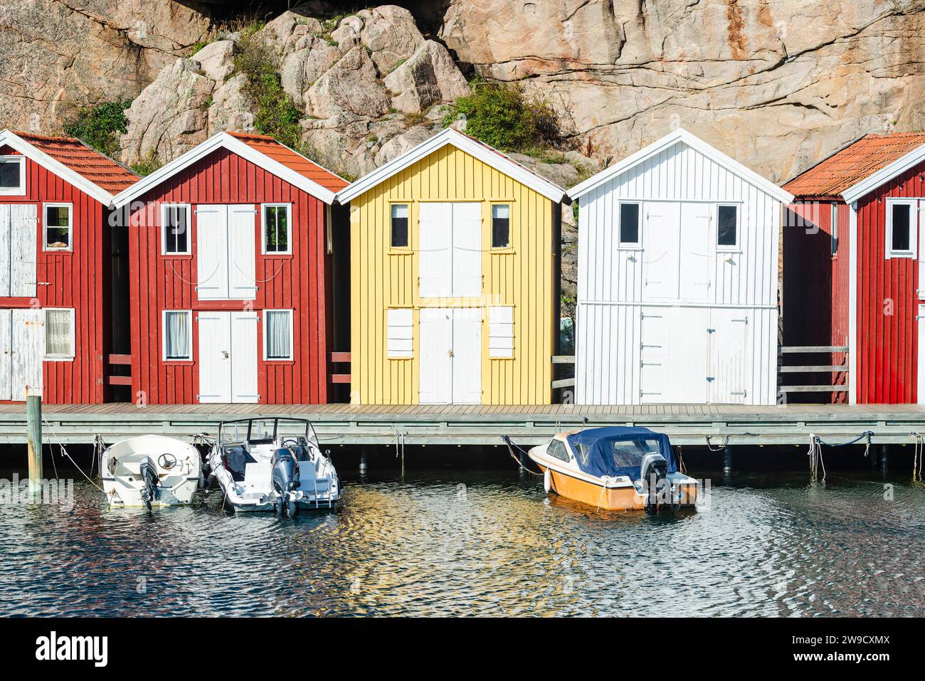 Capannoni per barche e magazzini con colorate facciate in legno e rocce di granito nel porto di Smögen, nell'arcipelago della costa occidentale svedese Foto Stock
