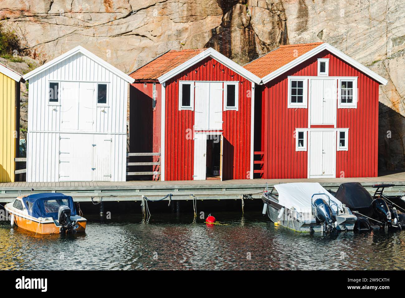 Capannoni per barche e magazzini con colorate facciate in legno e rocce di granito nel porto di Smögen, nell'arcipelago della costa occidentale svedese Foto Stock