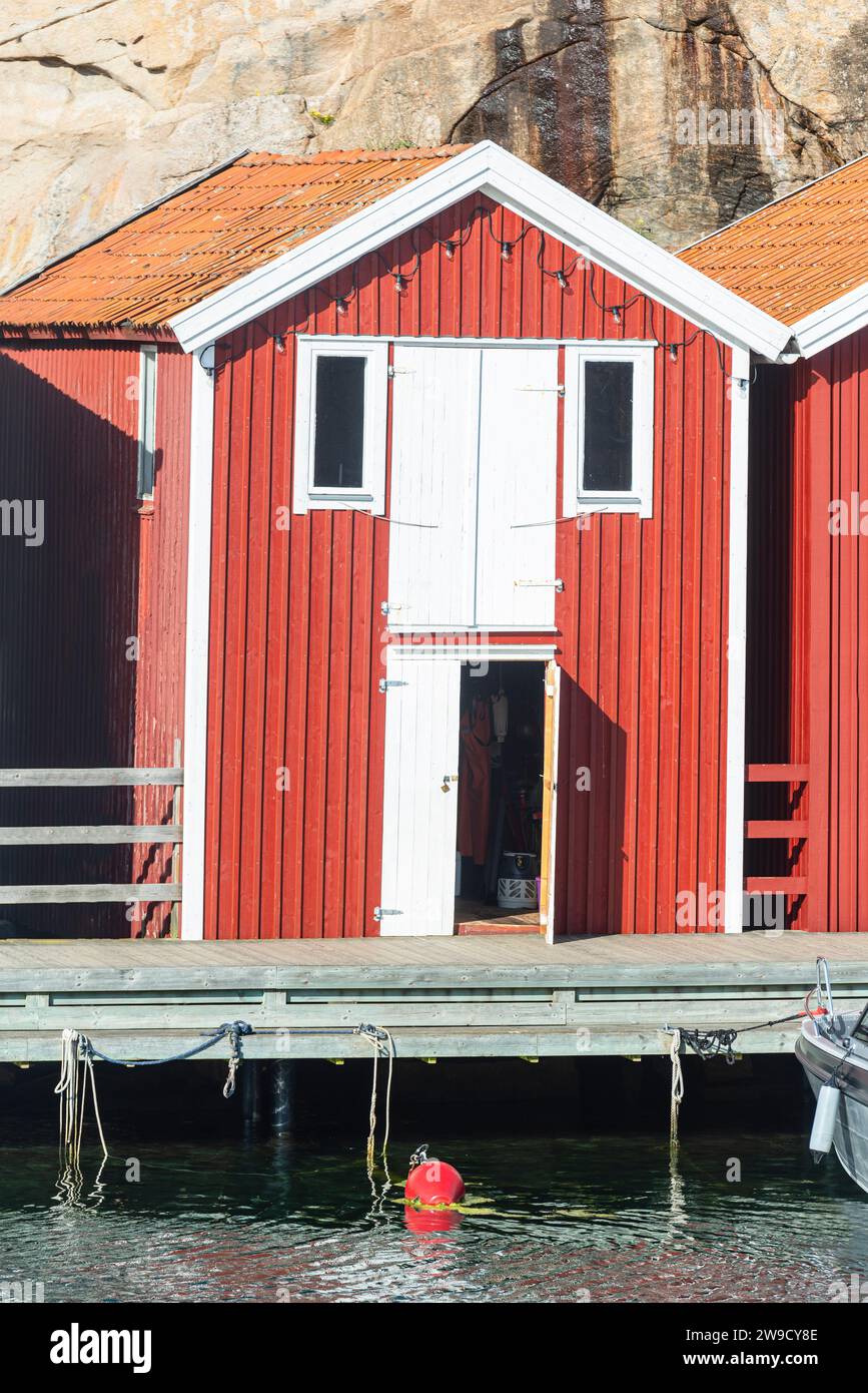 Magazzino con facciata in legno rosso davanti a rocce di granito sul lungomare del porto di Smögen, nell'arcipelago della costa occidentale svedese Foto Stock
