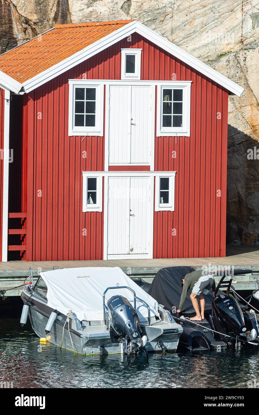 Magazzino con facciata in legno rosso davanti a rocce di granito sul lungomare del porto di Smögen, nell'arcipelago della costa occidentale svedese Foto Stock