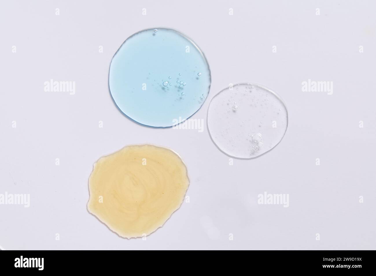 Liquidi trasparenti con vari colori adornati su sfondo bianco. Scena per pubblicizzare o mostrare le texture dei cosmetici. Spazio disponibile Foto Stock