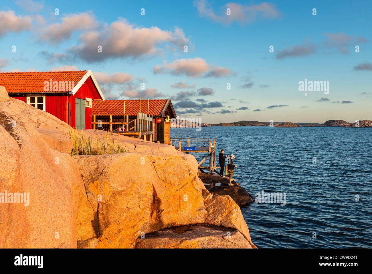 Le rocce di granito con le boathouses rosse nell'arcipelago della costa occidentale svedese brillano d'oro al tramonto Foto Stock