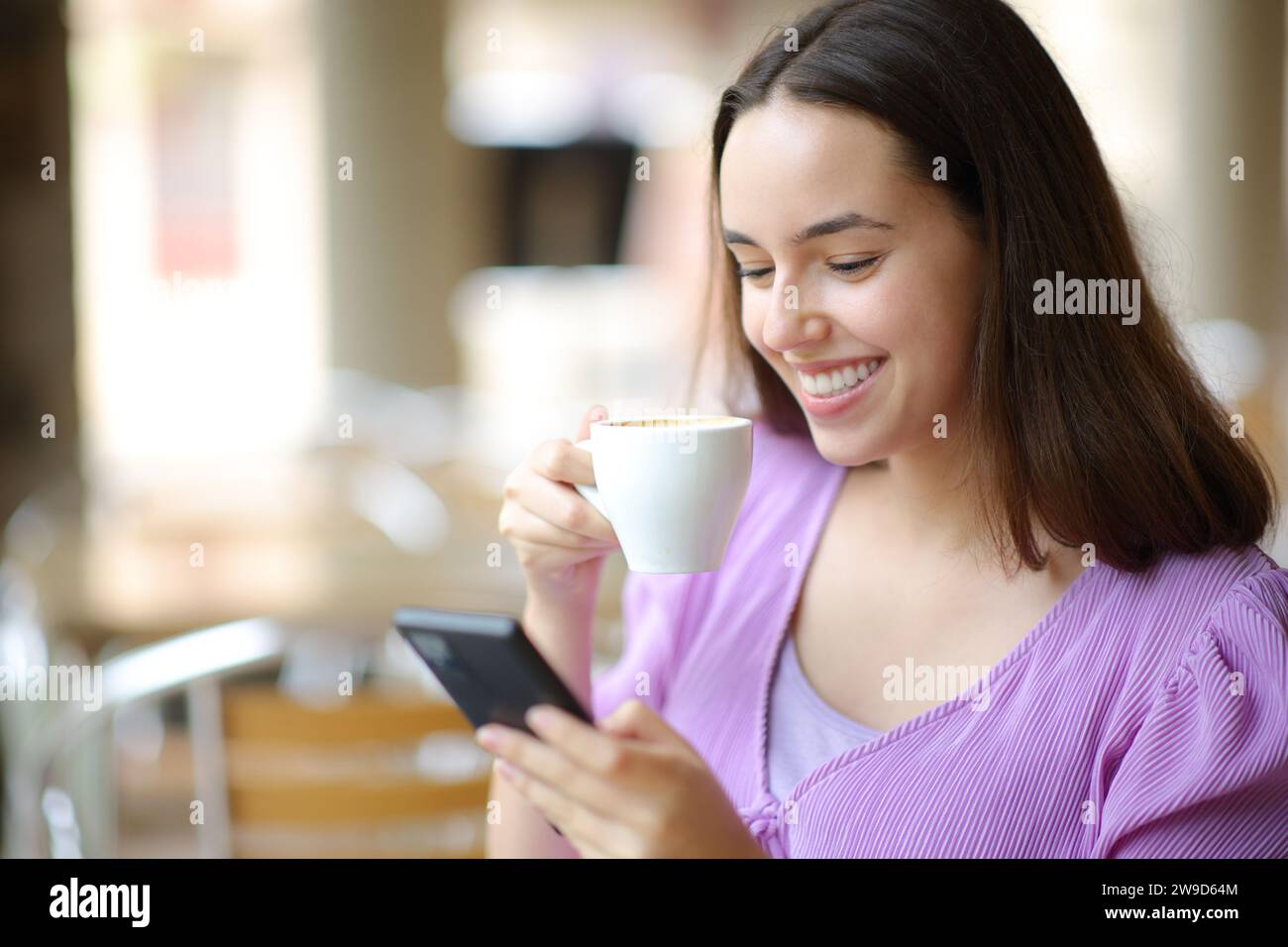 Una donna felice che beve caffè usando il telefono cellulare in una terrazza del ristorante Foto Stock