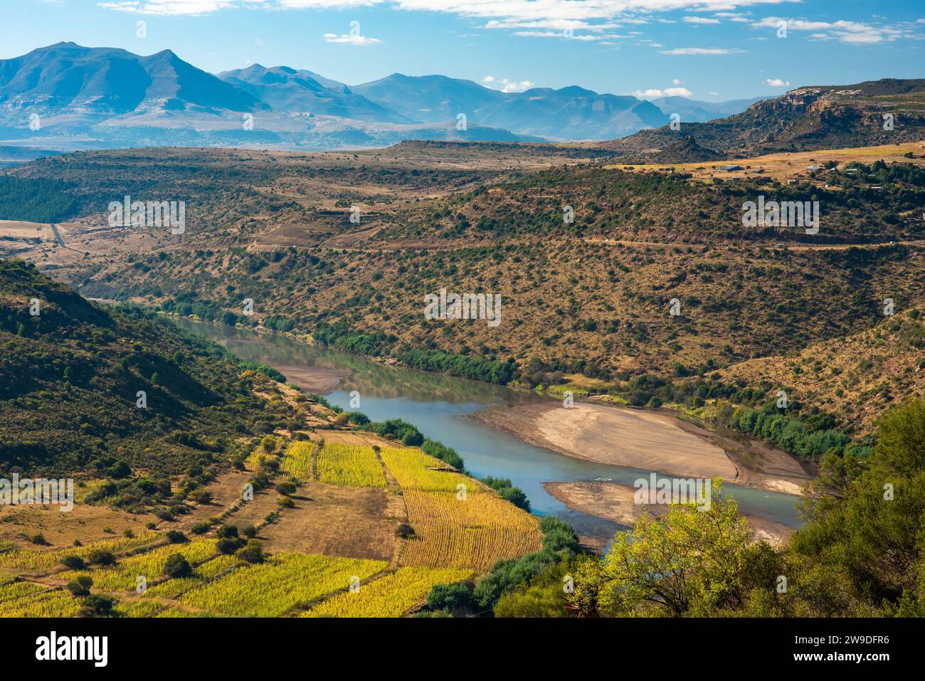 Un fiume scorre attraverso una valle nel Lesotho rurale, con fattorie sulle rive e montagne all'orizzonte Foto Stock