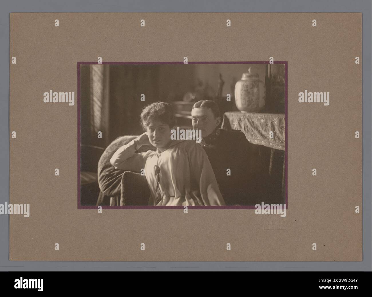 Ritratto di un uomo e di una donna, su un divano, all'interno, c. 1900 - c. 1920 Fotografia Ritratto di uomini e donne (seduti) in un soggiorno/studio, un suggestivo vaso ornamentale cinese sullo sfondo. Perforare e stampare in cartone, al centro della parte superiore. Foto su un piccolo cartone viola incollato su un cartone marrone. Confronta con la foto rp-f-00-6018: Lo stesso uomo e la stessa donna. Supporto fotografico Utrecht. stampa in argento gelatina di cartone Foto Stock