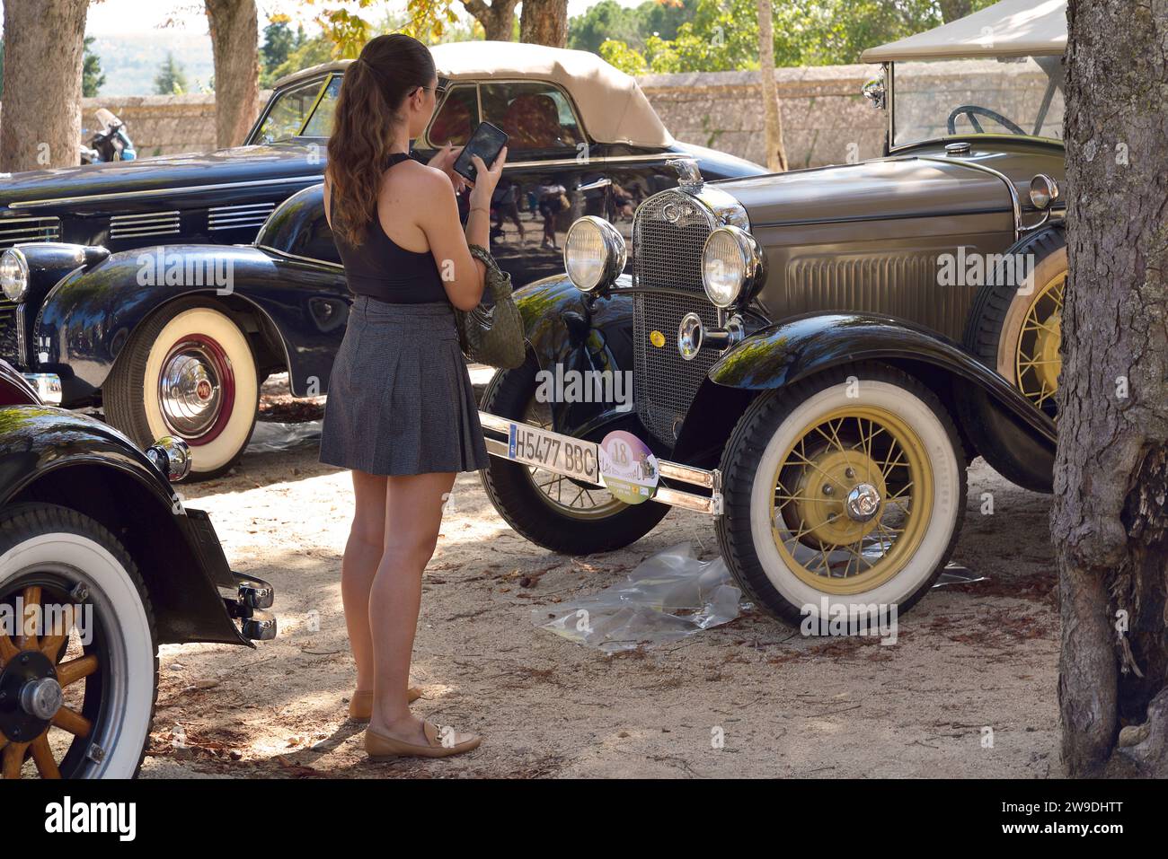 Una ragazza che scatta foto con il cellulare a un'auto d'epoca Ford in un festival automobilistico a San Lorenzo de El Escorial, Madrid. Foto Stock