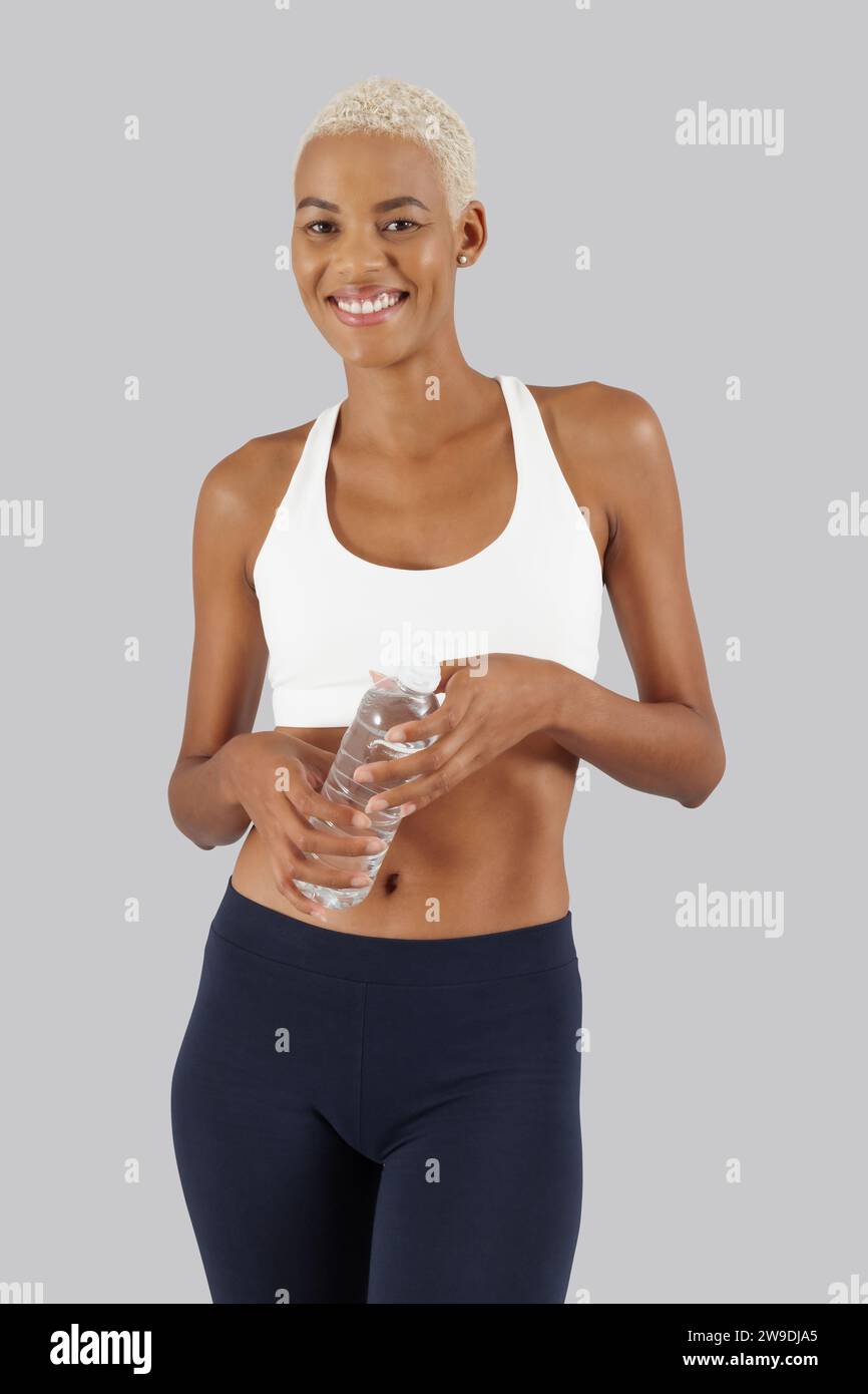 Allenamento fitness, donna sorridente con bottiglia d'acqua, atleta afro-americana in abbigliamento sportivo, atleta sportiva fare esercizio in palestra per impr Foto Stock