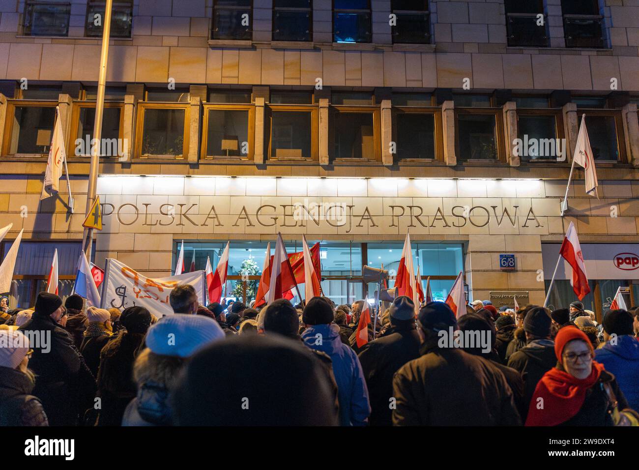La gente sventola le bandiere nazionali polacche al di fuori della sede polacca dell'agenzia di stampa polacca, di proprietà statale, pap, a Varsavia, in Polonia, il 26 dicembre 2023. Le persone si sono riunite al di fuori dello studio statale TVP e dell'agenzia di stampa polacca pap nella protesta in corso contro la mossa della nuova coalizione pro-europea di reimporre l'integrità e l'obiettività nei media pubblici. Varsavia Polonia dimostrazione in difesa di TVP. 2023/12/26 Copyright: XMarekxAntonixIwanczukx MAI08673-Enhanced-NR Foto Stock