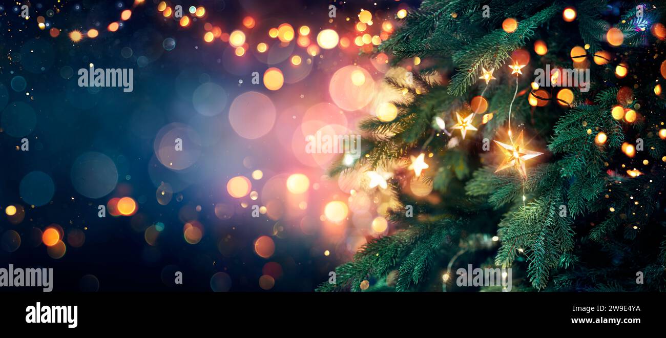 Albero di Natale con luci in blu - stelle appese ai rami di Fir con scintillanti e bokeh in sfondo astratto sfocato Foto Stock