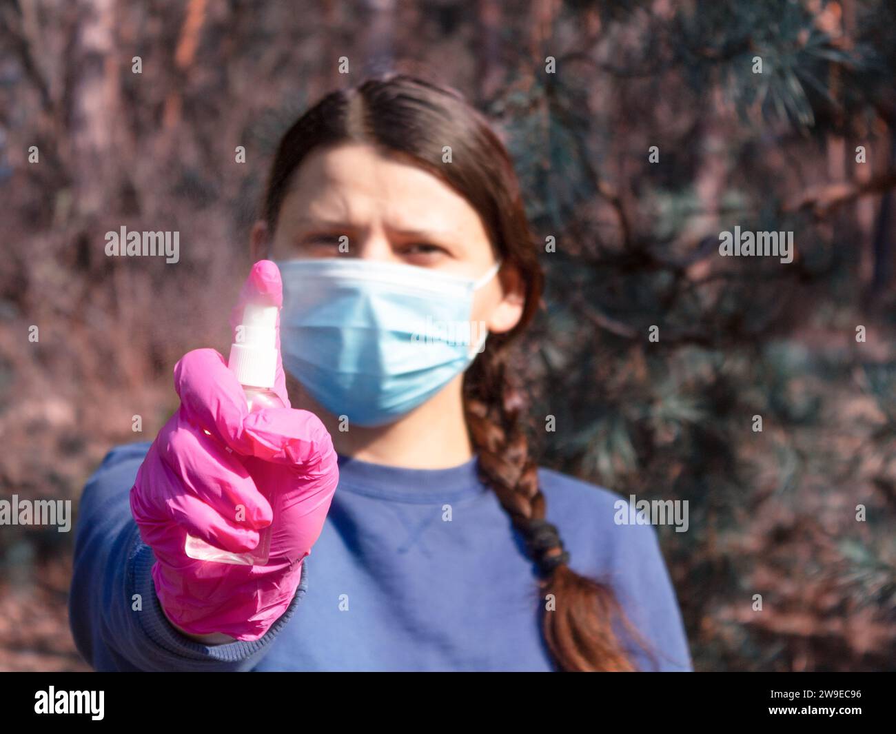 Ragazza in una maschera protettiva medica e guanti spruzzato uno spray antisettico. Concetto di pandemia di coronavirus. Foto Stock
