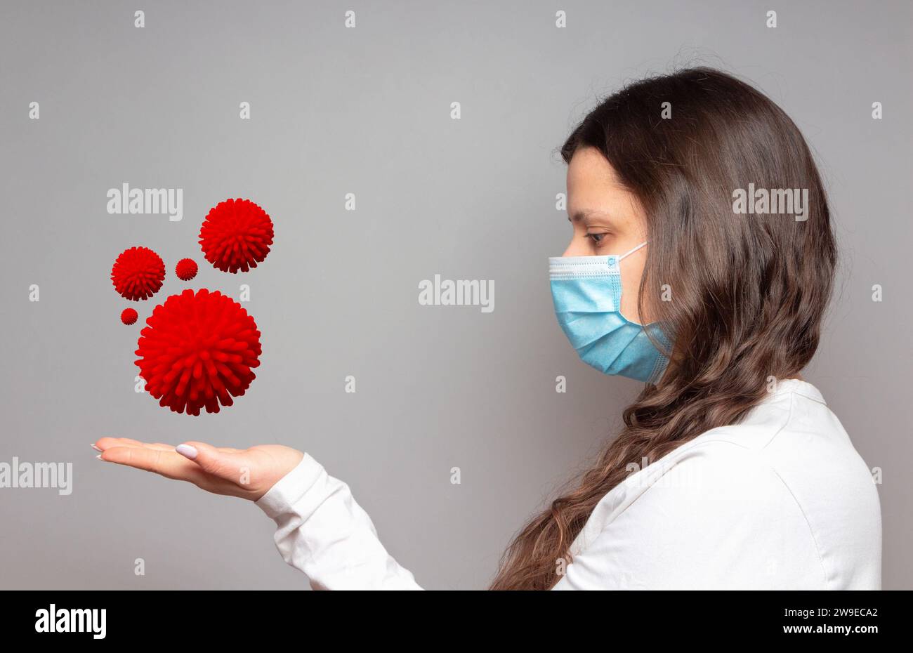 Ragazza in maschera protettiva medica tiene sul palmo i batteri Covid -19. Concetto di pandemia di coronavirus. Foto Stock