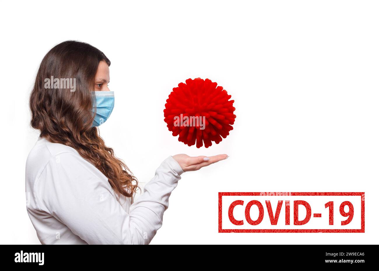 Il concetto di lotta contro il Covid-19. Una ragazza con una maschera medica protettiva tiene un batterio coronavirus sui palmi. Foto Stock