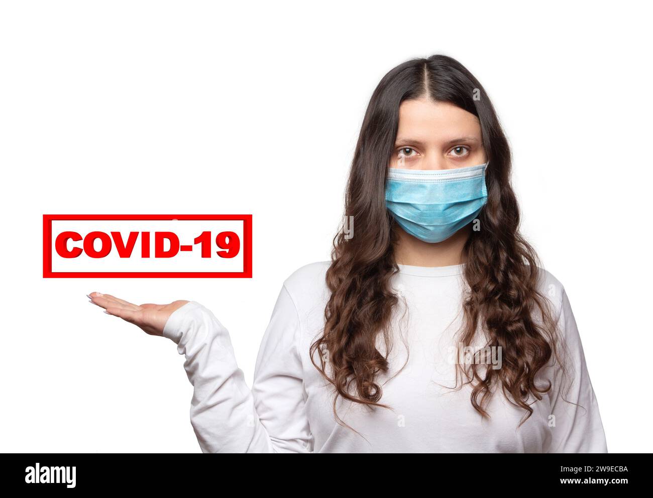 COVID-19. Una ragazza con una maschera medica protettiva tiene sulla mano il testo rosso Coronavirus su sfondo bianco. Foto Stock