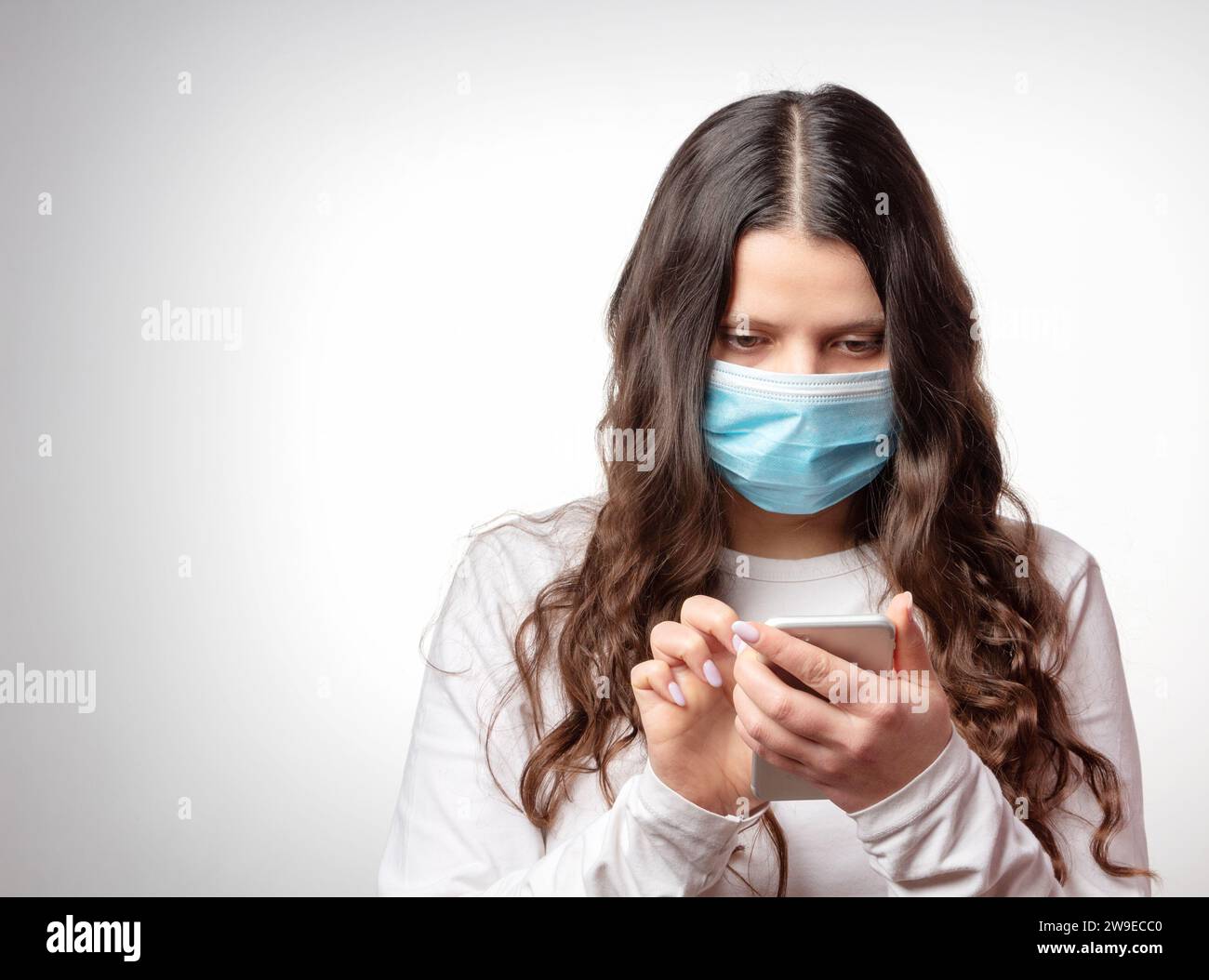 COVID-19. Una ragazza con una maschera protettiva sta scrivendo un messaggio in uno smartphone. Pandemia di coronavirus. Epidemia di nCoV. Foto Stock