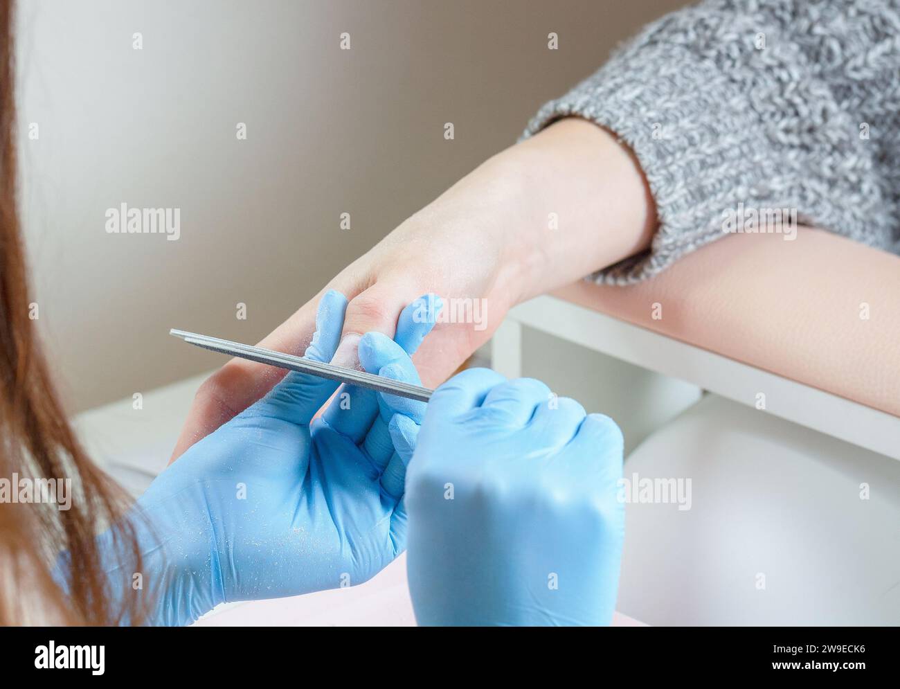 Manicurista con guanti blu per levigare le unghie con lima per unghie in un salone di bellezza. Foto Stock