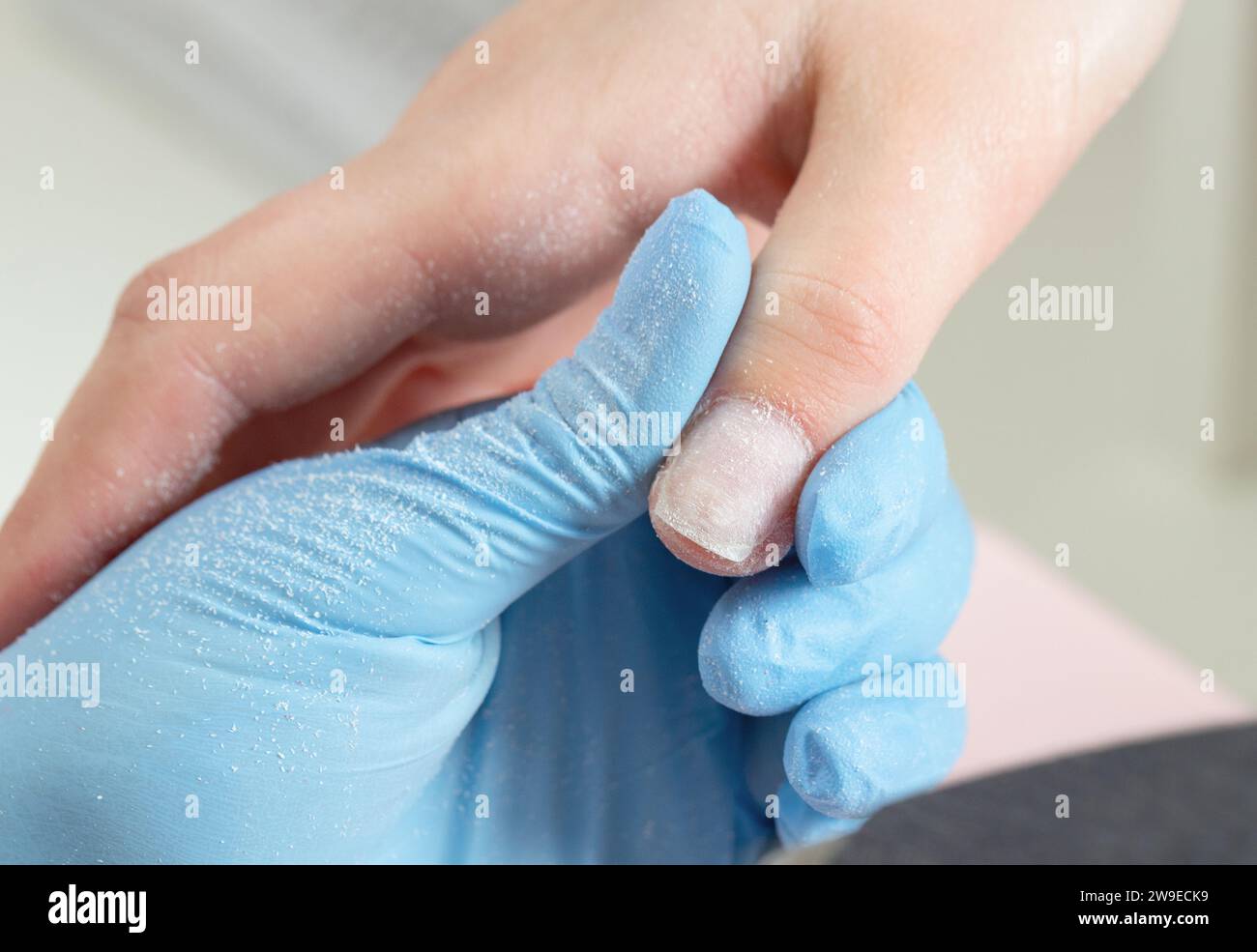 Processo di manicure nel salone di bellezza. Manicurista in guanti blu tiene il dito con un'unghia lucida. Foto Stock