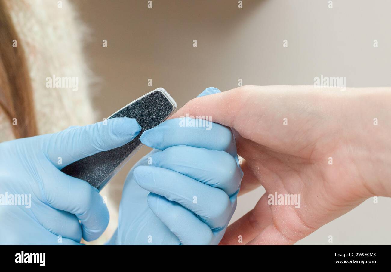 Manicurista con guanti blu leviga un'unghia con una lima per unghie in un salone di bellezza. Foto Stock