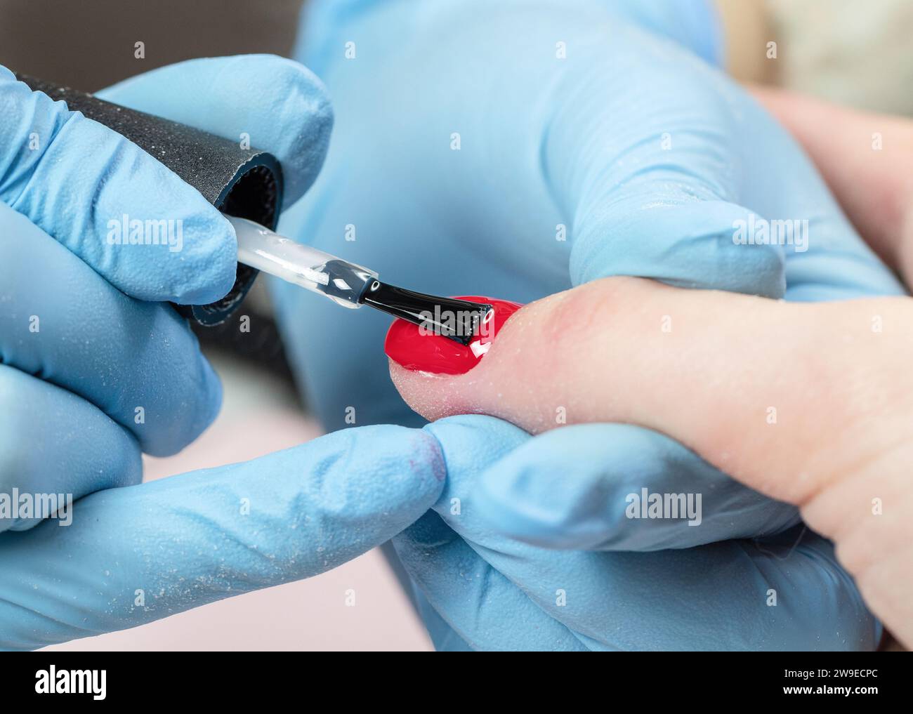 Manicurista in guanti blu che ricoprono l'unghia con smalto gel. Processo di manicure in un salone di bellezza da vicino. Foto Stock