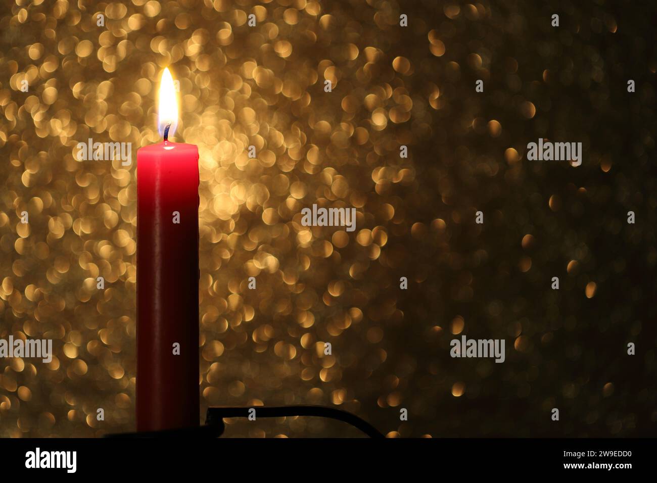 Primo piano di una candela a bastone rossa su uno sfondo dorato scintillante, spazio di copia Foto Stock