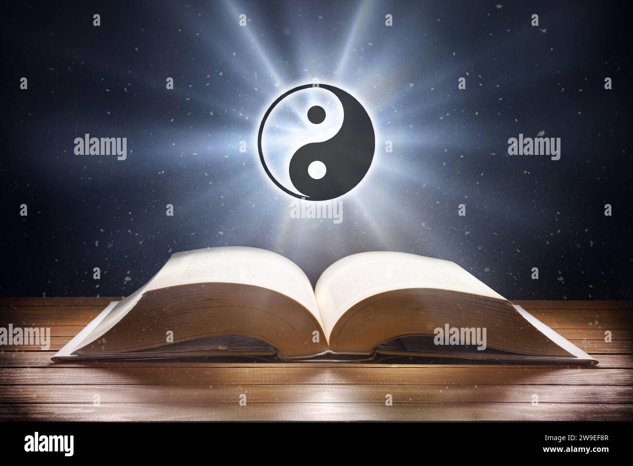 Libro aperto su un tavolo di legno e simbolo taoista con fascio di luce su sfondo scuro. Vista frontale. Foto Stock