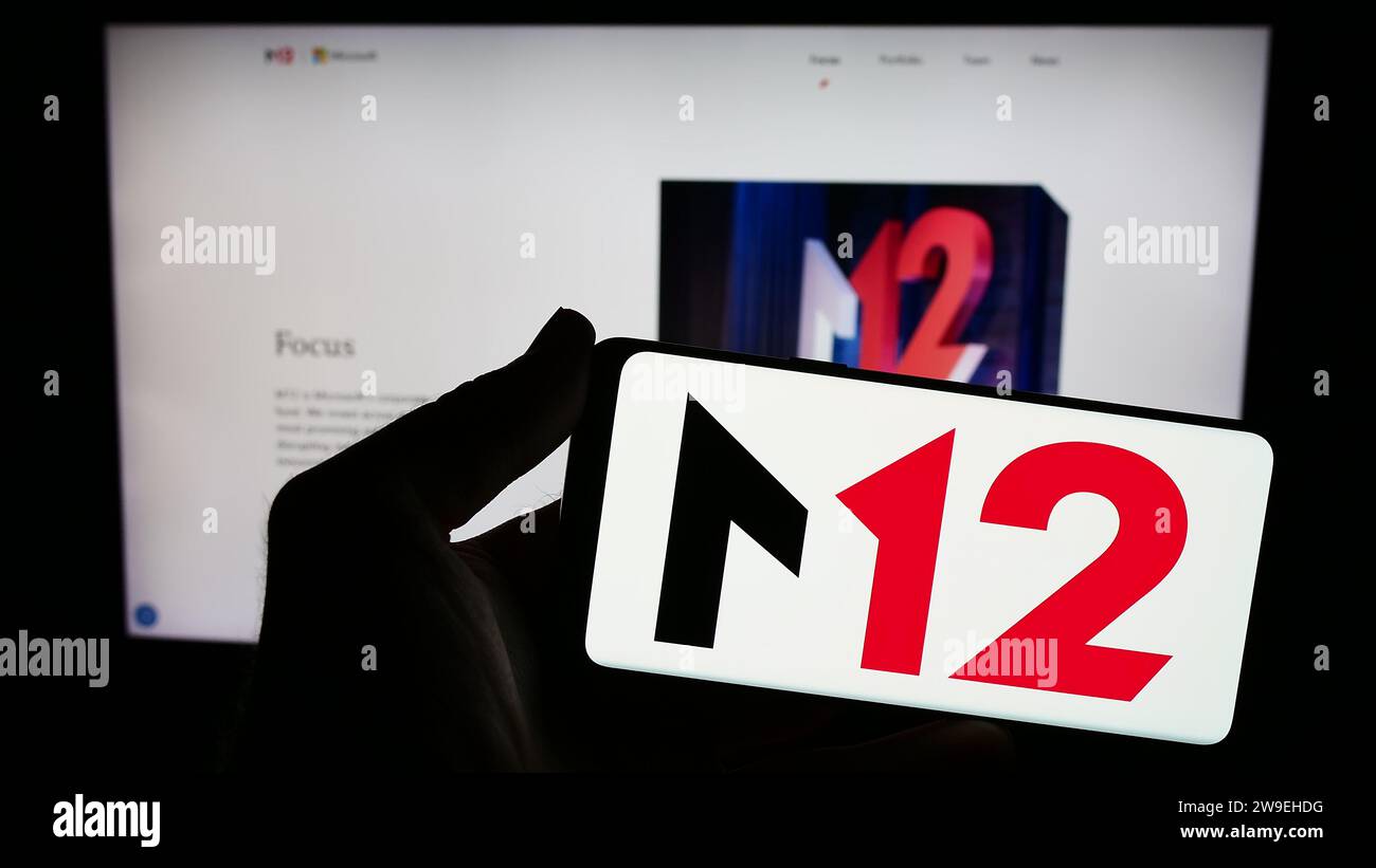 Persona che possiede uno smartphone con il logo della società statunitense di venture capital M12 (Microsoft) davanti al sito Web. Concentrarsi sul display del telefono. Foto Stock