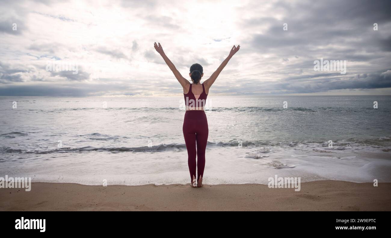 donna sportiva in piedi al mare con le braccia alzate per festeggiare, allontanandosi da tutto. Foto Stock