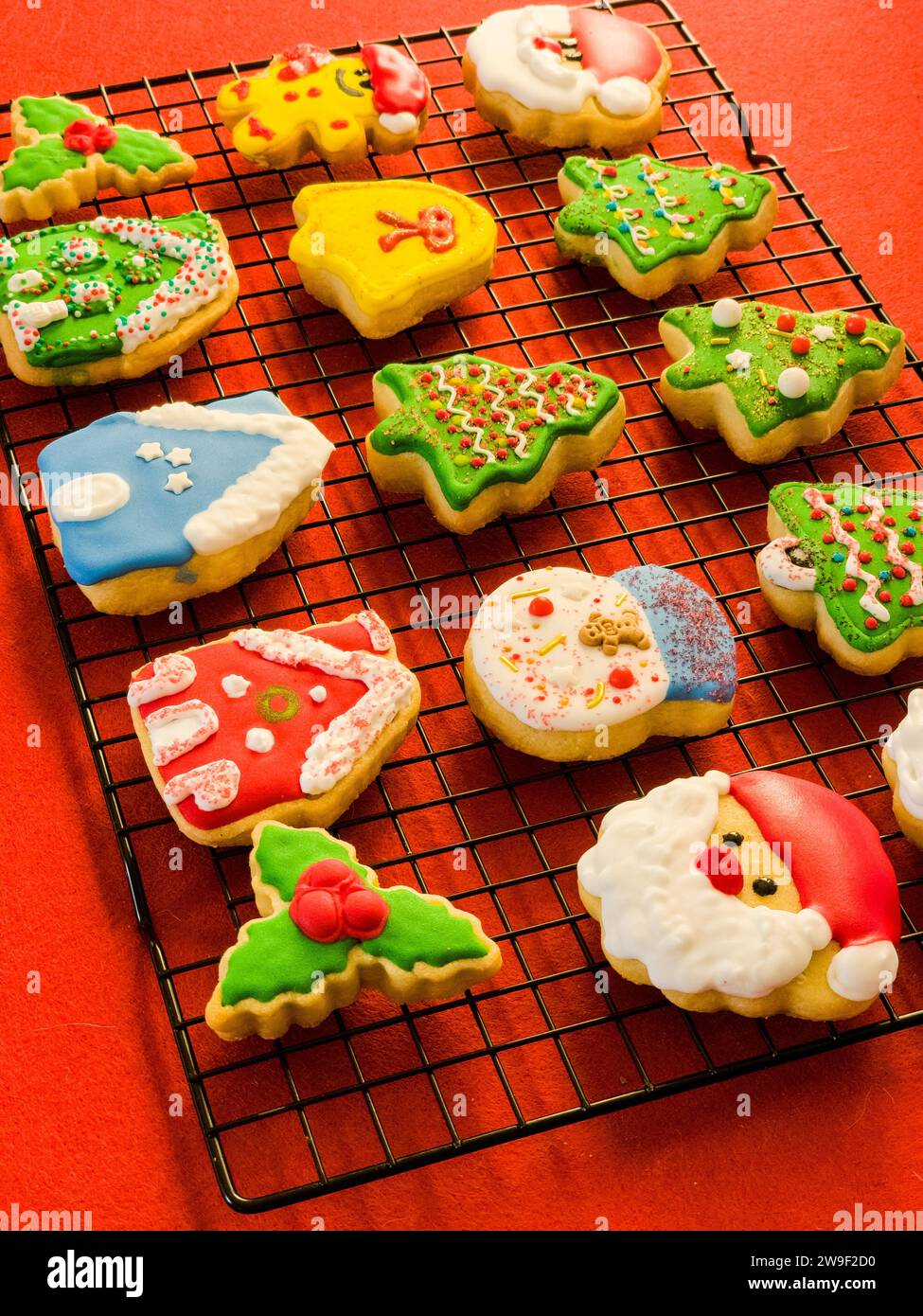 Una colorata esposizione di biscotti di zucchero a tema natalizio è presentata su una griglia metallica contro un ripiano arancione Foto Stock
