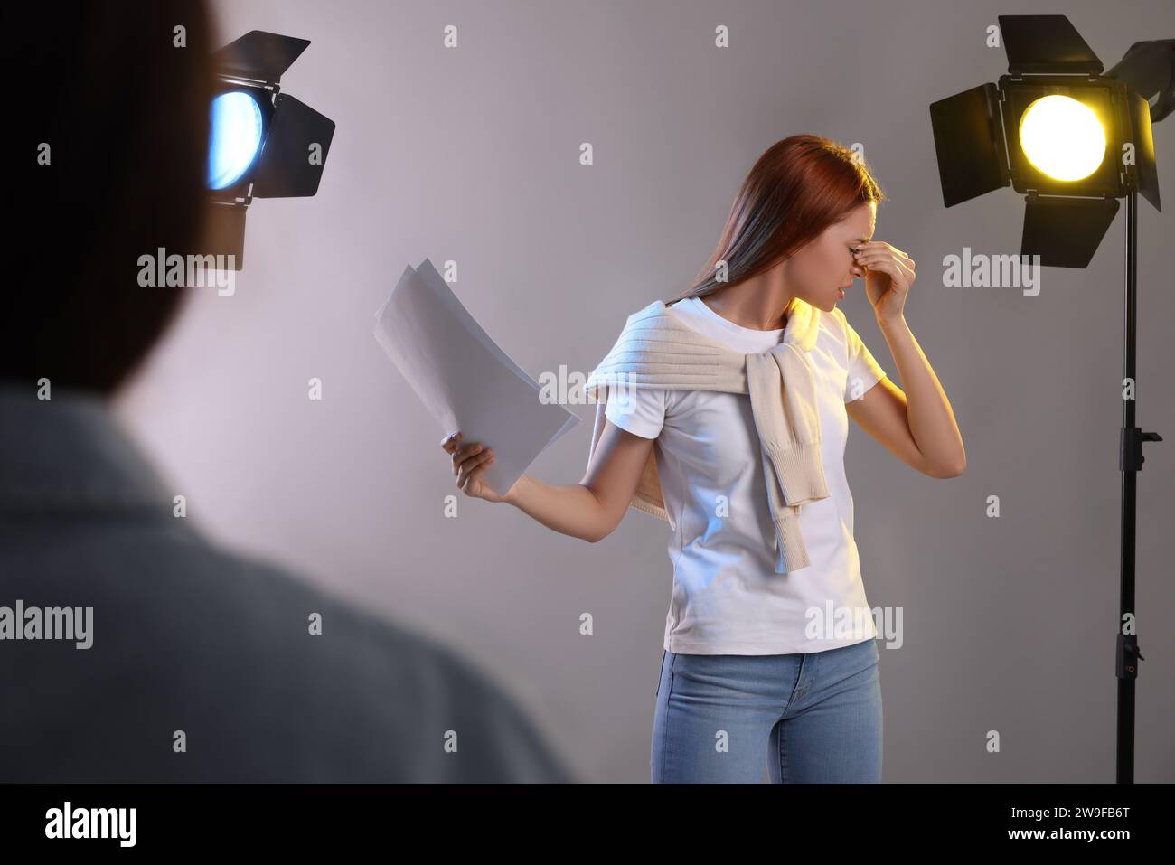 Donna emotiva con sceneggiatura che si esibisce di fronte al direttore del casting su sfondo grigio allo studio Foto Stock