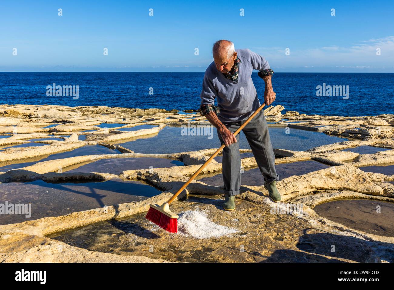 Żaren Darmanin, coltivatore di sale a Malta, dimostra la raccolta del sale nelle sue saline a Marsaskala. Saline di Darmanin vicino a Marsascala, Malta Foto Stock