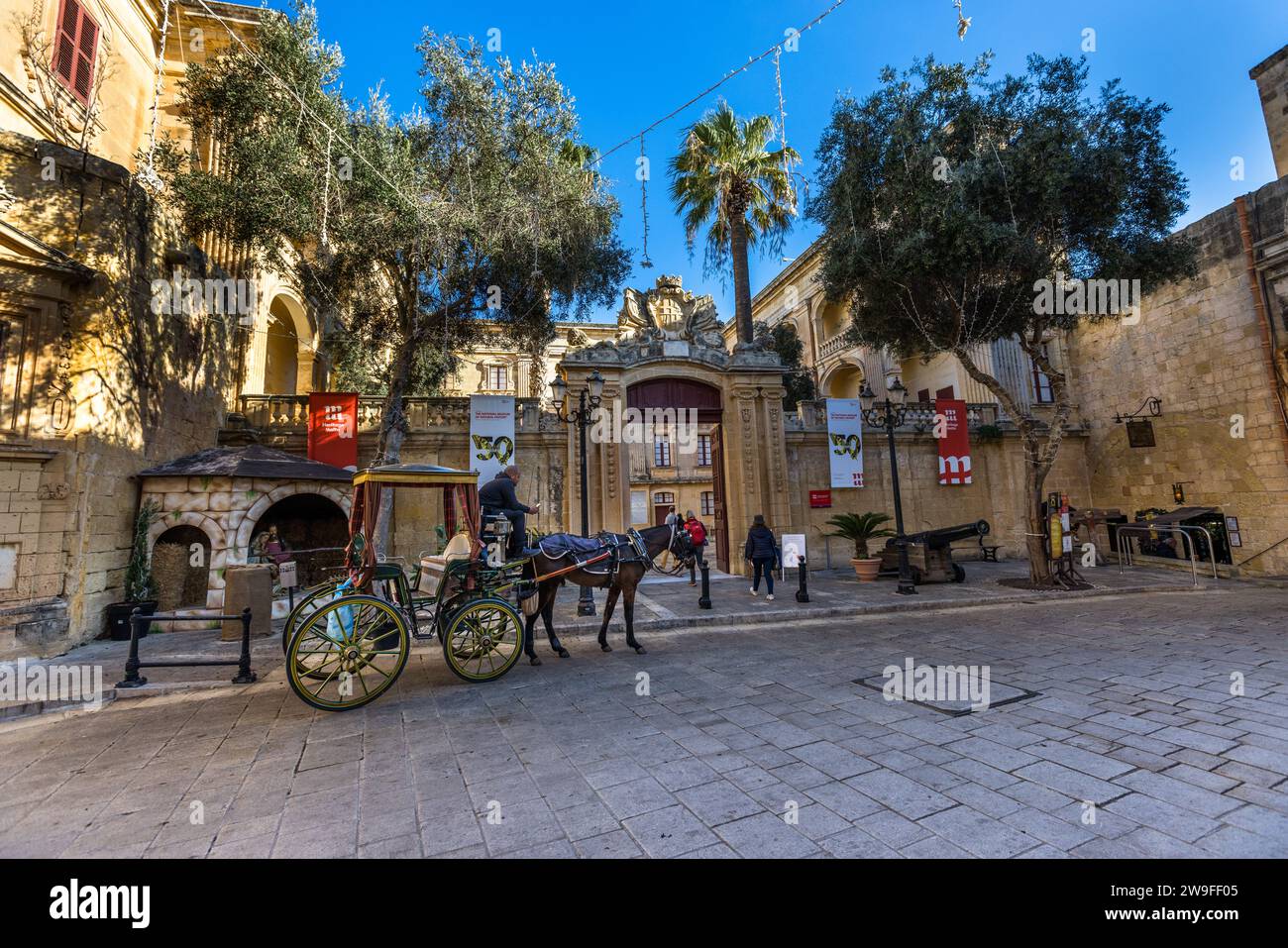 Una karozzin aspetta davanti al portale barocco del Palazzo Vilhena a Mdina, che ospita il Museo Nazionale di Storia Naturale dal 1973. Due cannoni storici affiancano l'ingresso. Questo cortile antistante è stato tra i luoghi utilizzati a Mdina per la prima stagione di Game of Thrones nel 2011. Foto Stock