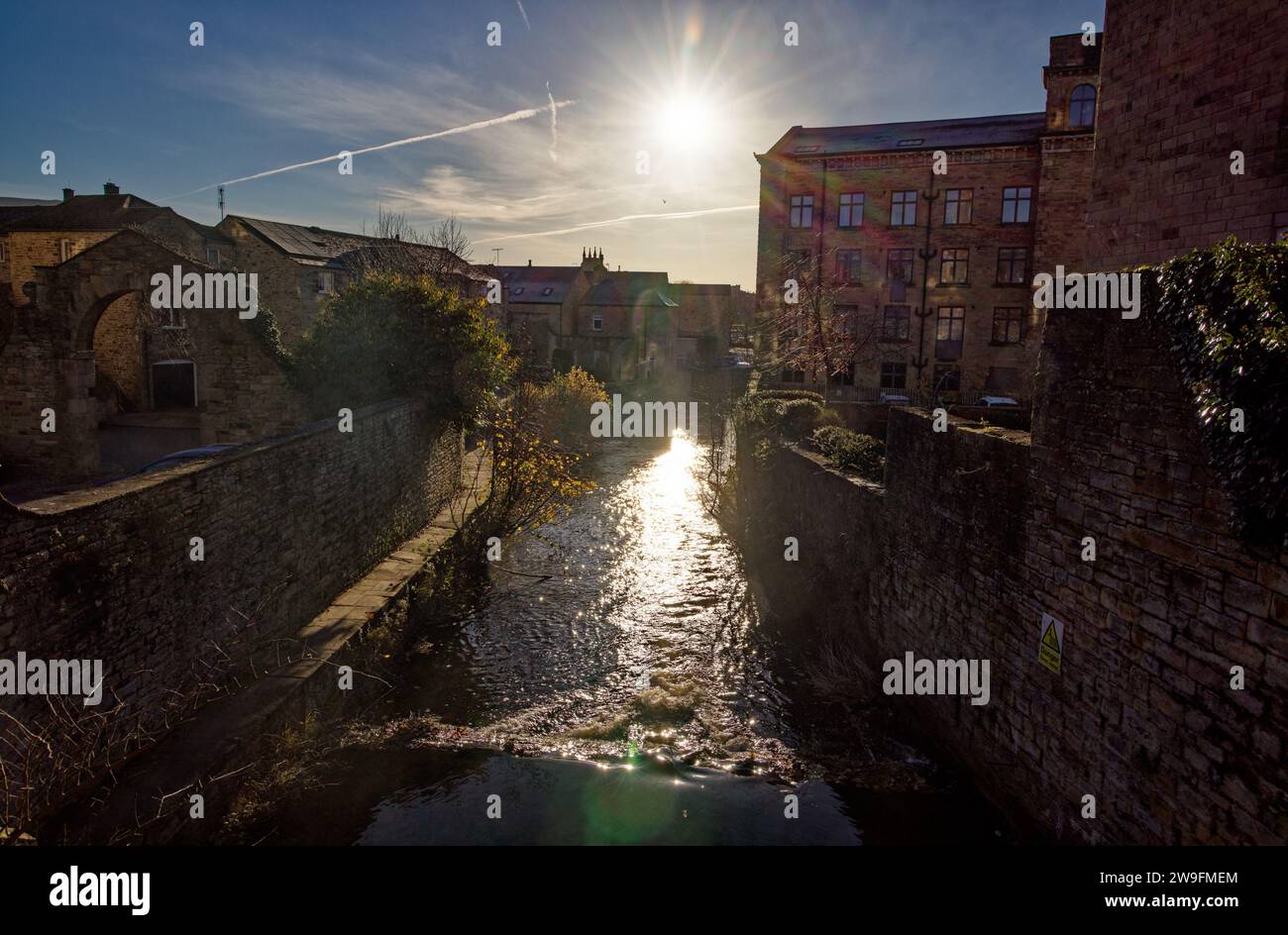 Un piccolo fiume attraversa un paesaggio urbano di edifici industriali storici convertiti lungo l'Eller Beck, Skipton, North Yorkshire. Foto Stock