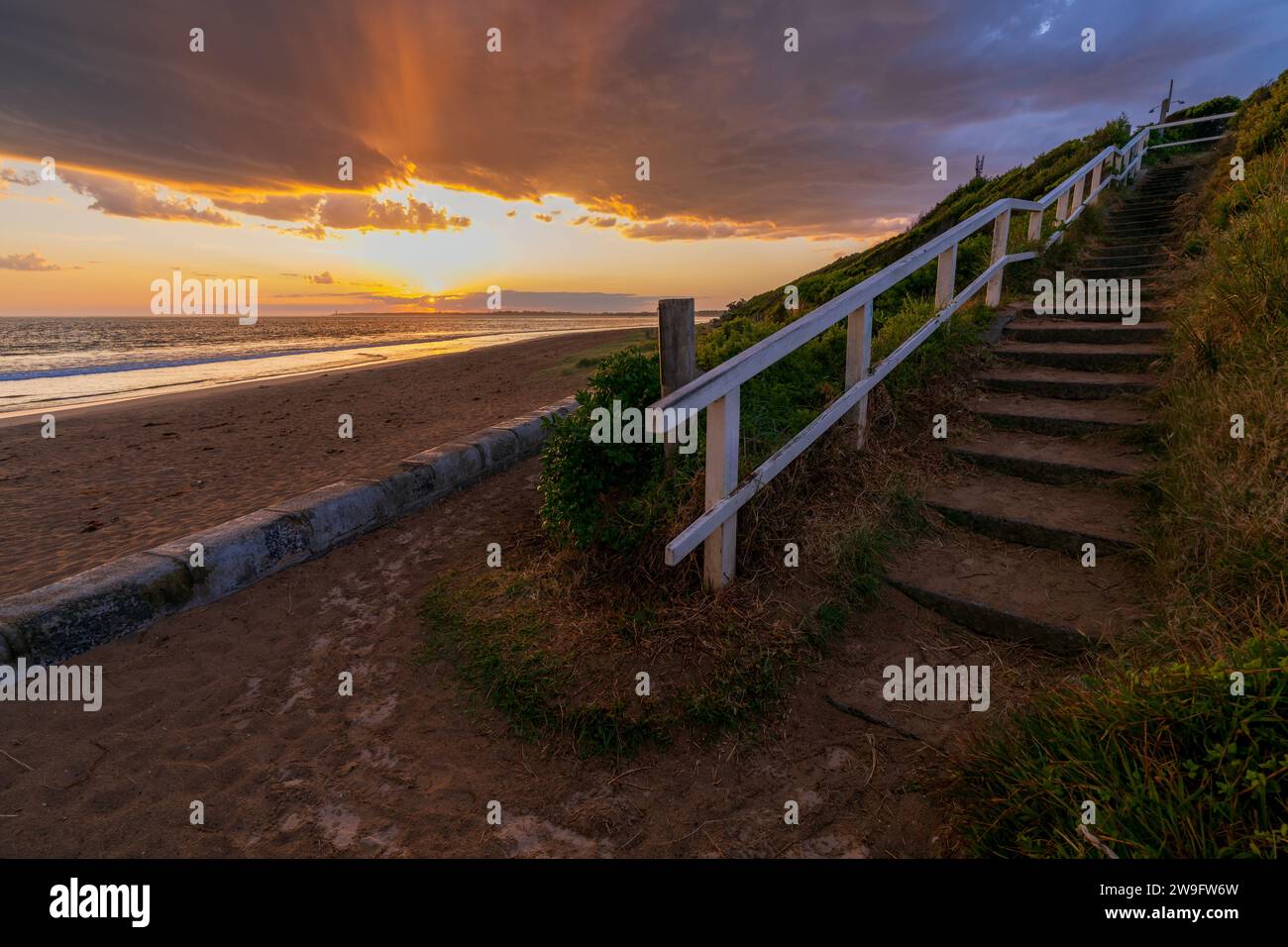 Un tramonto colorato su una serie di gradini giù per una spiaggia di sabbia a Queenscliff sulla penisola di Bellarine a Victoria, Australia. Foto Stock