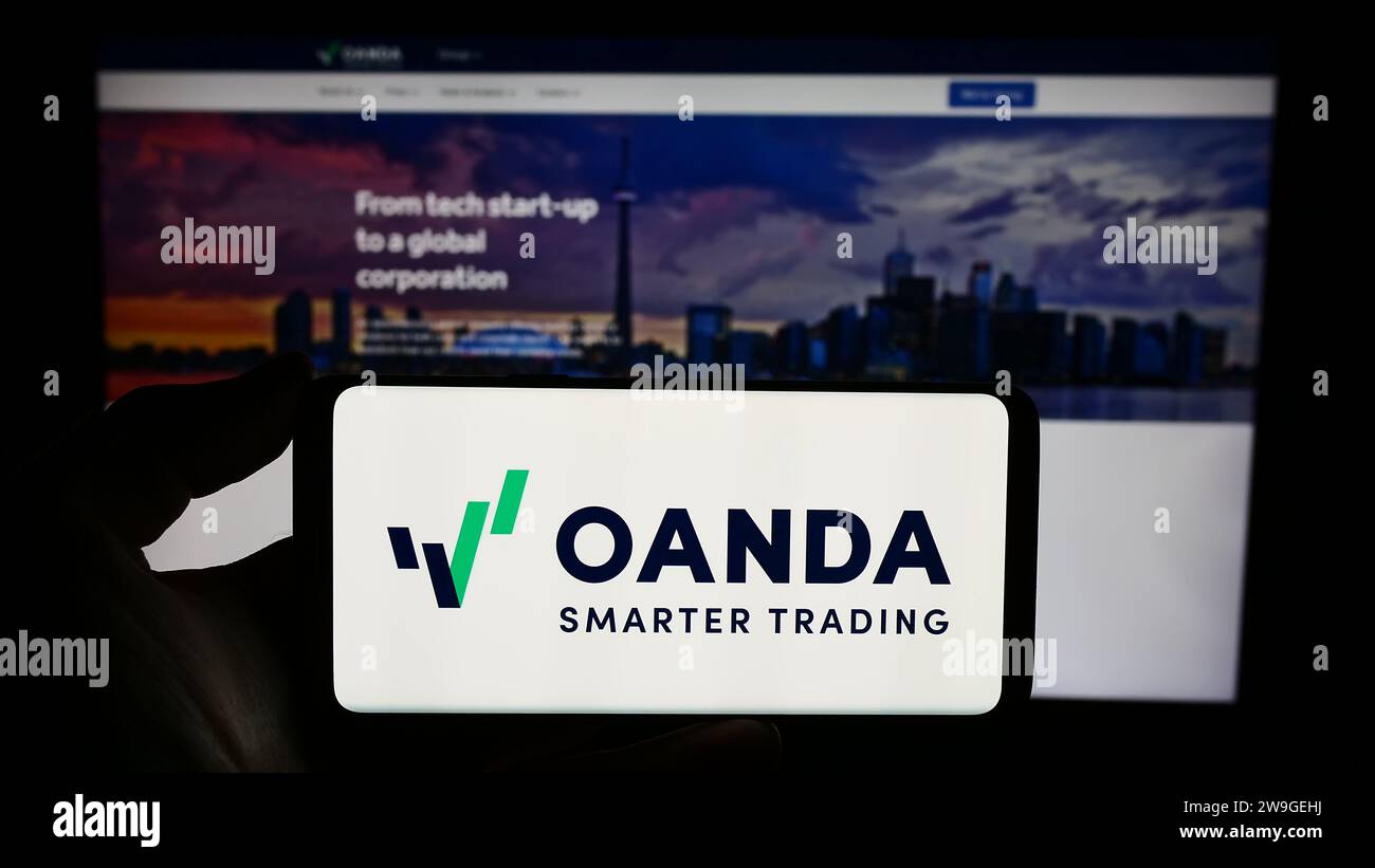 Persona che possiede uno smartphone con il logo della società statunitense OANDA Business Information Services Inc. Davanti al sito Web. Concentrarsi sul display del telefono. Foto Stock