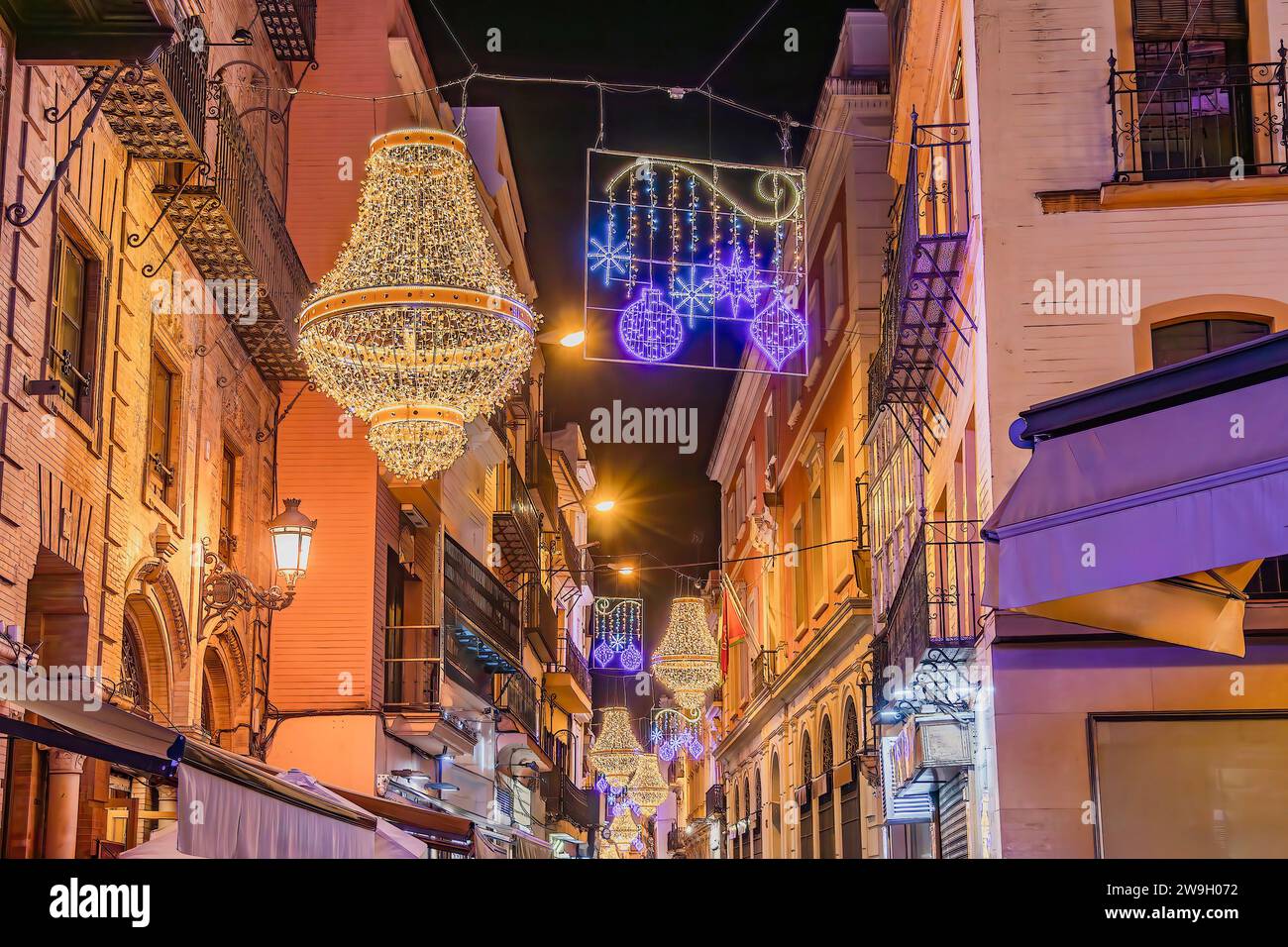 Siviglia, Spagna - 16 dicembre 2023: Decorazione di luci natalizie in via Sierpes a forma di candelabro in cristallo in stile impero d'oro, a Siviglia Foto Stock