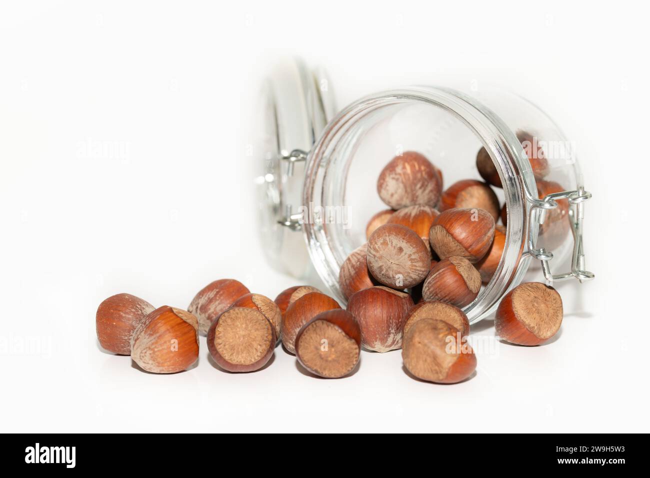 Primo piano delle nocciole fuoriuscite da un vaso rovesciato. I dadi e il vaso di conservazione sono tagliati su uno sfondo di colore chiaro. Foto Stock