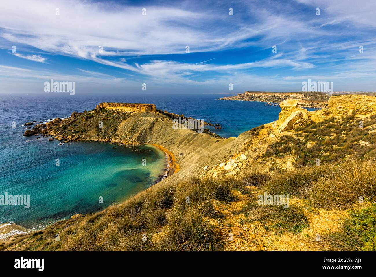 Baia di Għajn Tuffieħa con la roccia di il-Qarraba. Spiaggia di sabbia scura, famosa per il surf e situata in una baia circondata da colline, con un sentiero costiero vicino a L-Imġarr, Malta Foto Stock